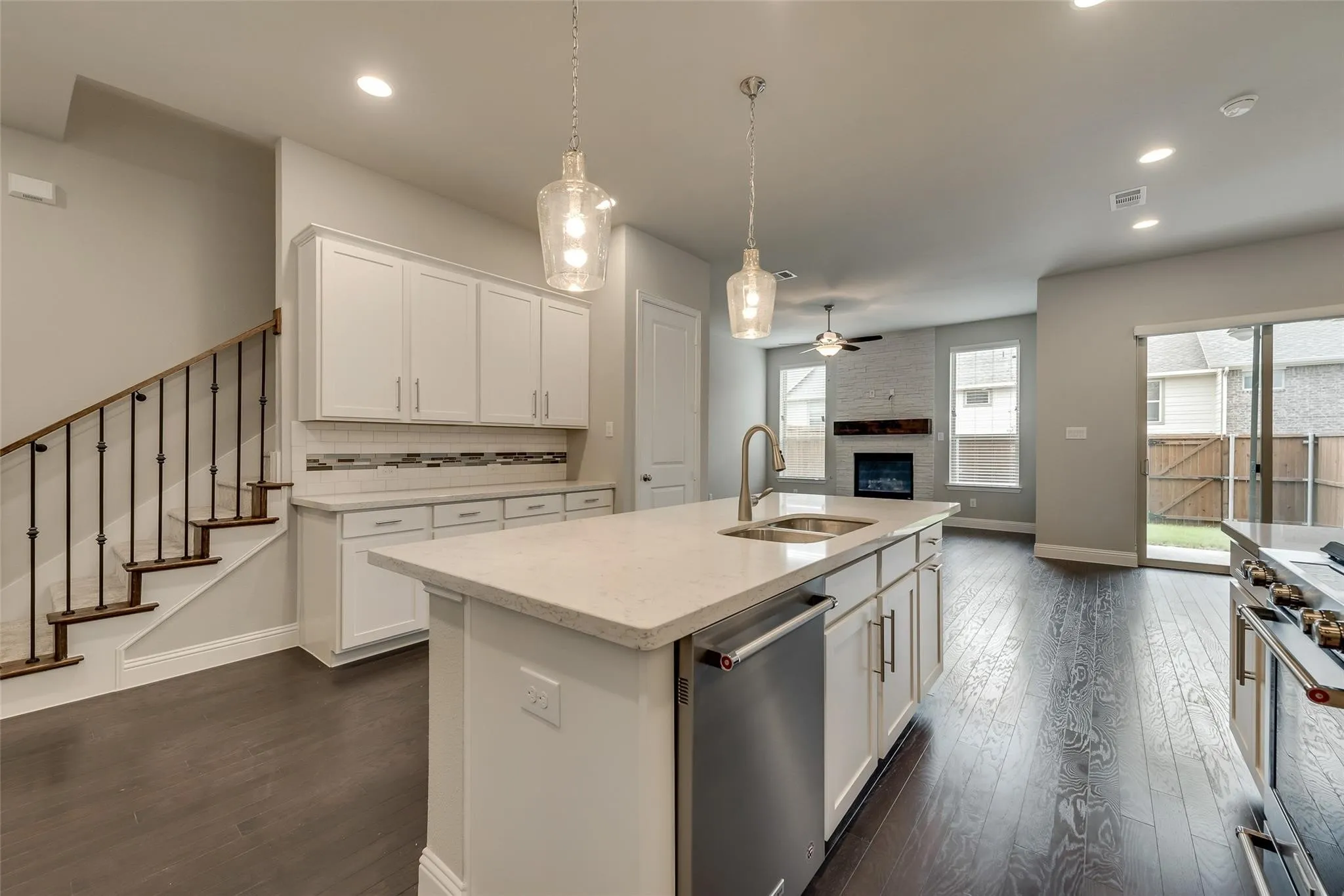 Wood-finish flooring throughout, kitchen island with integrated sink, stainless steel appliances, white cabinetry with modern hardware, and a fireplace with a stone surround