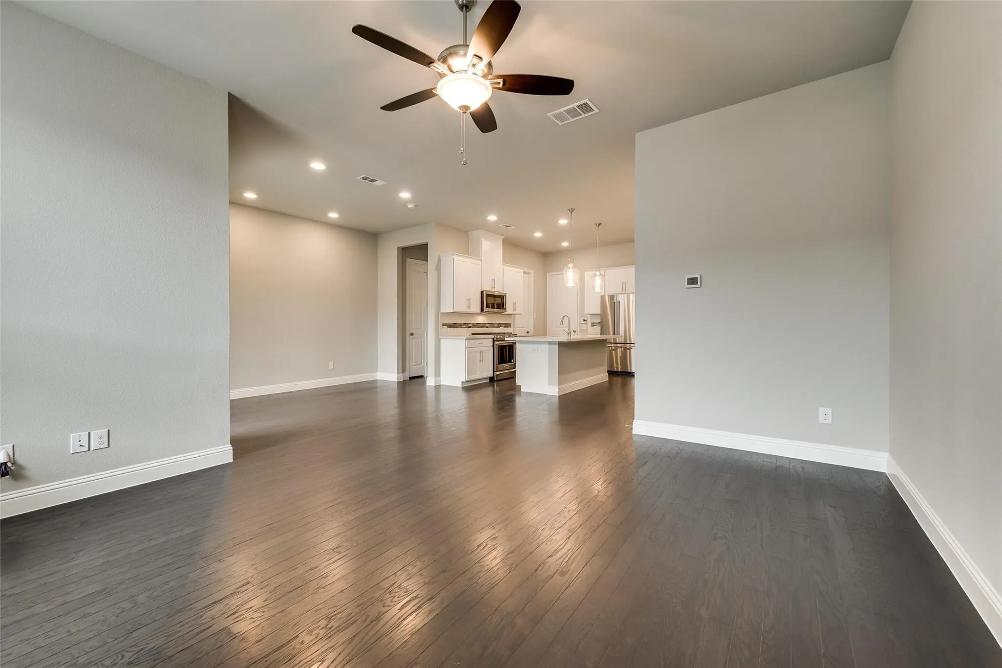 Expansive living area with dark wood-finish flooring, a ceiling fan with integrated lighting, and recessed ceiling lights