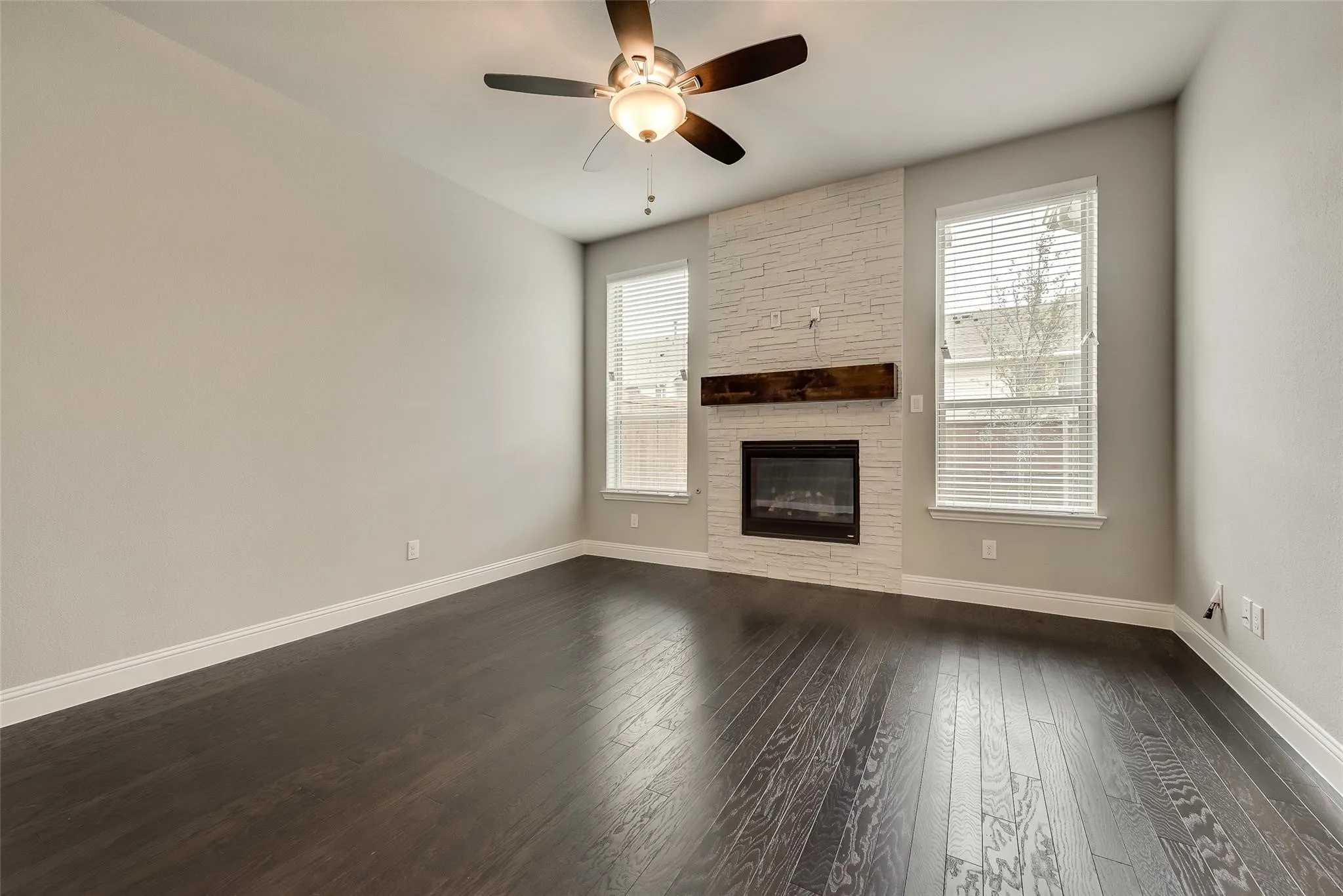 Wood-finish flooring, white brick fireplace surround, dark wood mantel, built-in fireplace, and ceiling fan with integrated lighting