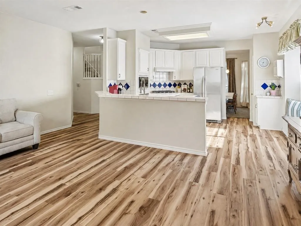 Wood-finish flooring throughout, kitchen with white cabinetry, tile countertops, and stainless steel appliances