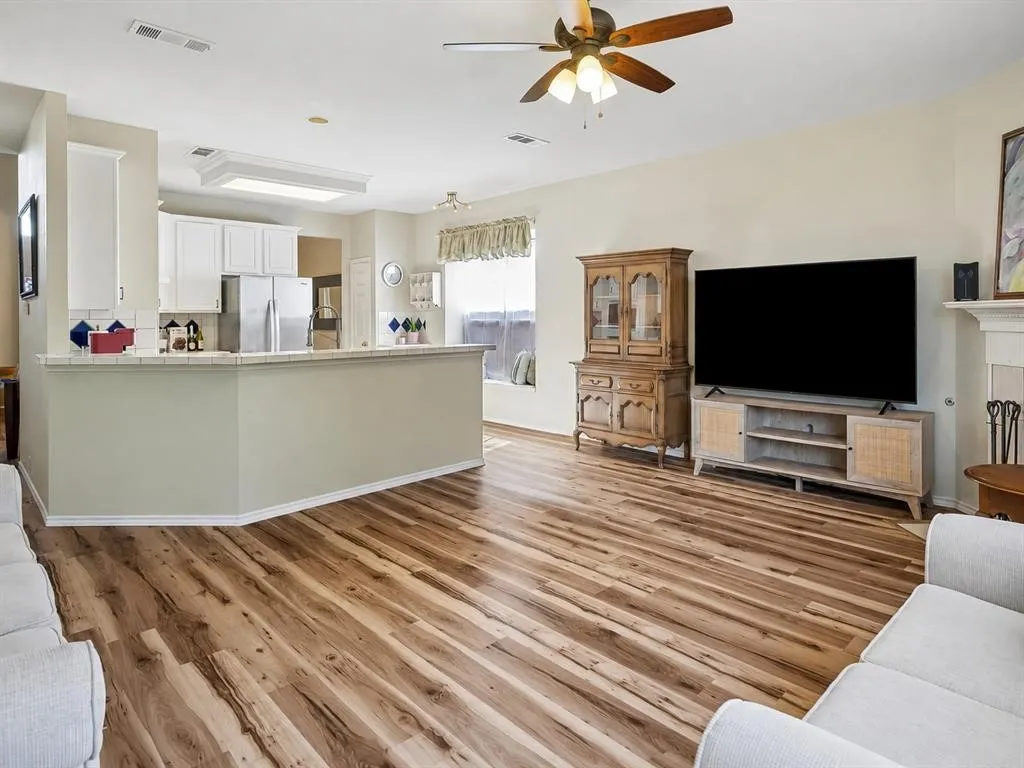 Wood-finish flooring throughout, white kitchen cabinetry, stainless steel refrigerator, and a ceiling fan with integrated lighting