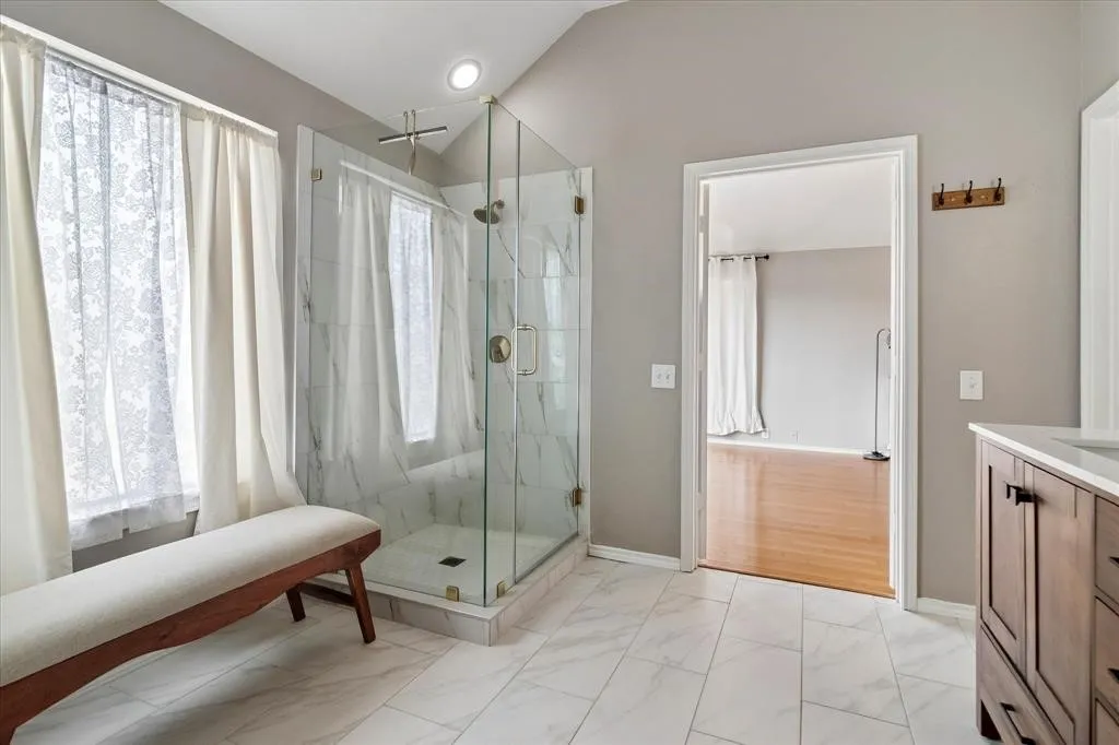 Glass-enclosed shower with white tiled walls and floor, vaulted ceiling, recessed lighting, and a dark wood-finish vanity with white countertop
