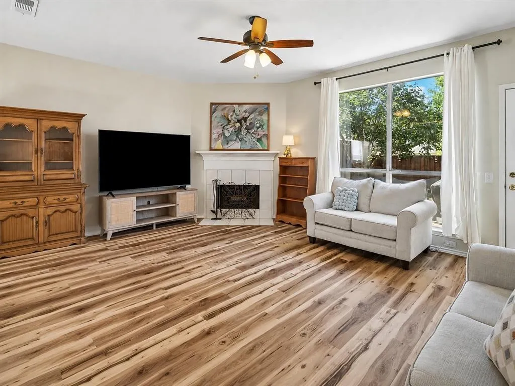 Spacious living area featuring wood-finish flooring, a ceiling fan, and a fireplace with a white mantel