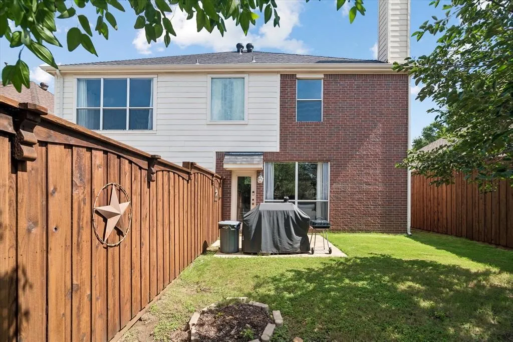 Private fenced backyard featuring a patio area, manicured lawn, and mature foliage