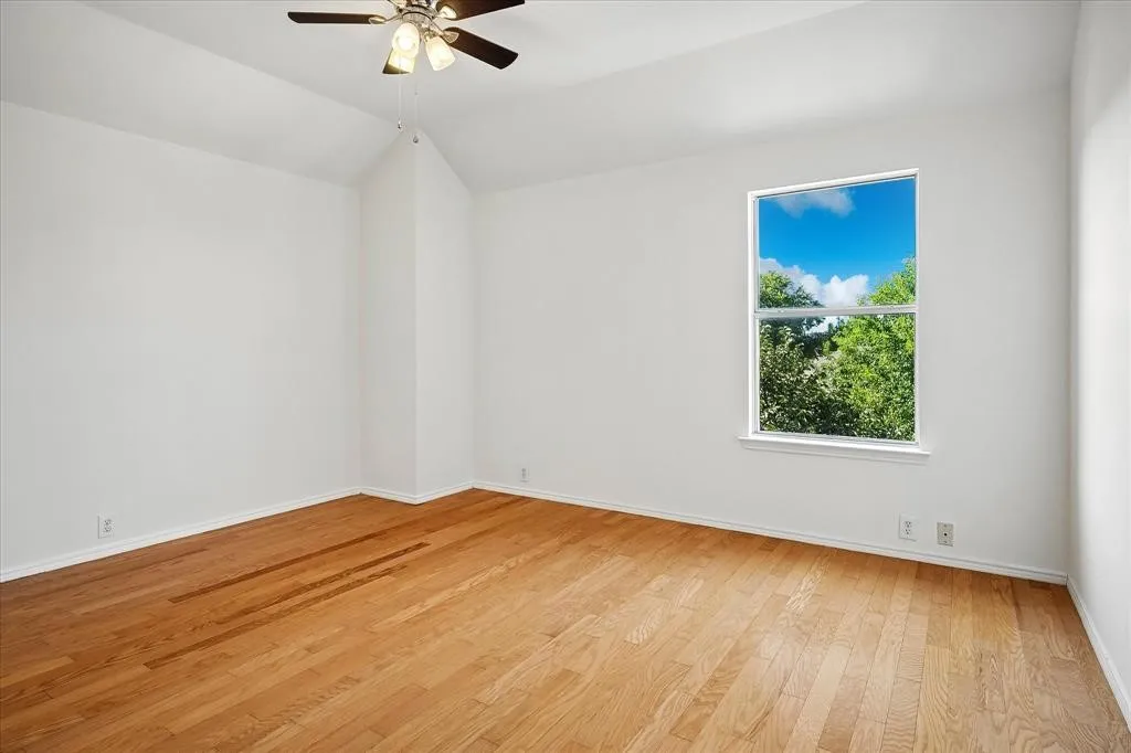 Vaulted ceiling with a ceiling fan, hardwood flooring, and a large window