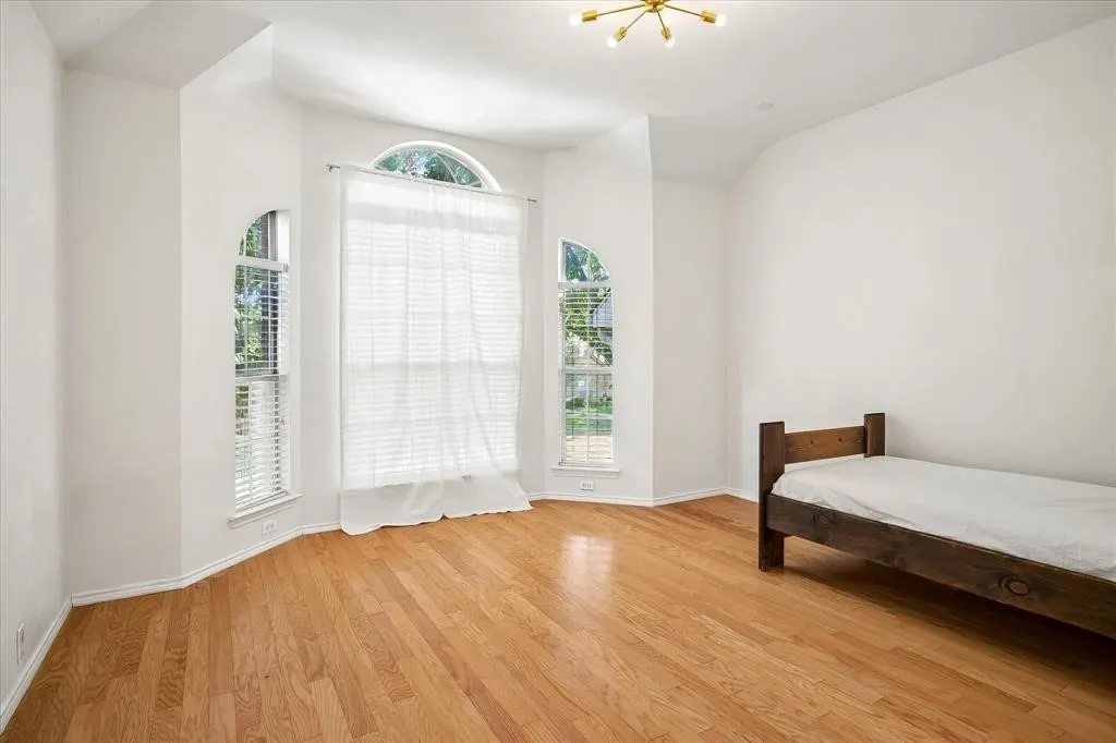Hardwood flooring, arched windows, vaulted ceiling, recessed window alcove, and contemporary ceiling light fixture