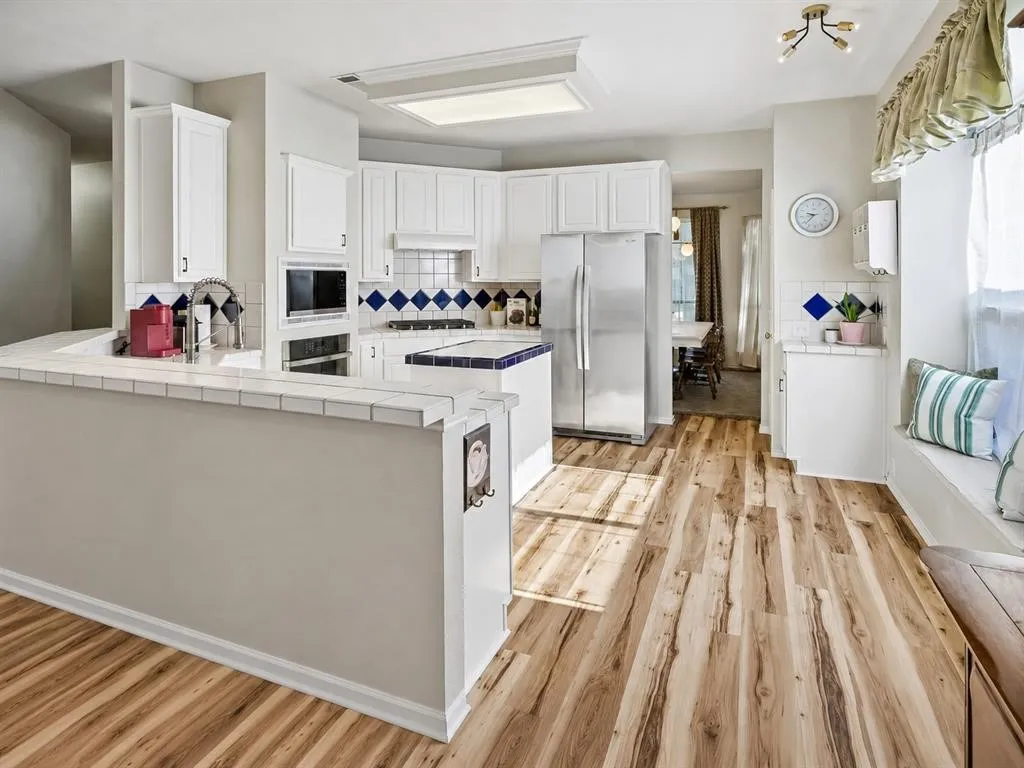 Kitchen featuring wood-finish flooring, white cabinetry, a built-in microwave, and stainless steel refrigerator