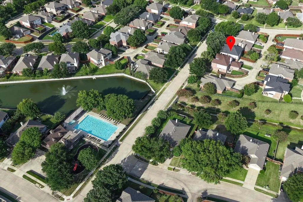Aerial perspective of a residential neighborhood featuring a central pond with fountain, a community swimming pool, and surrounding residential structures