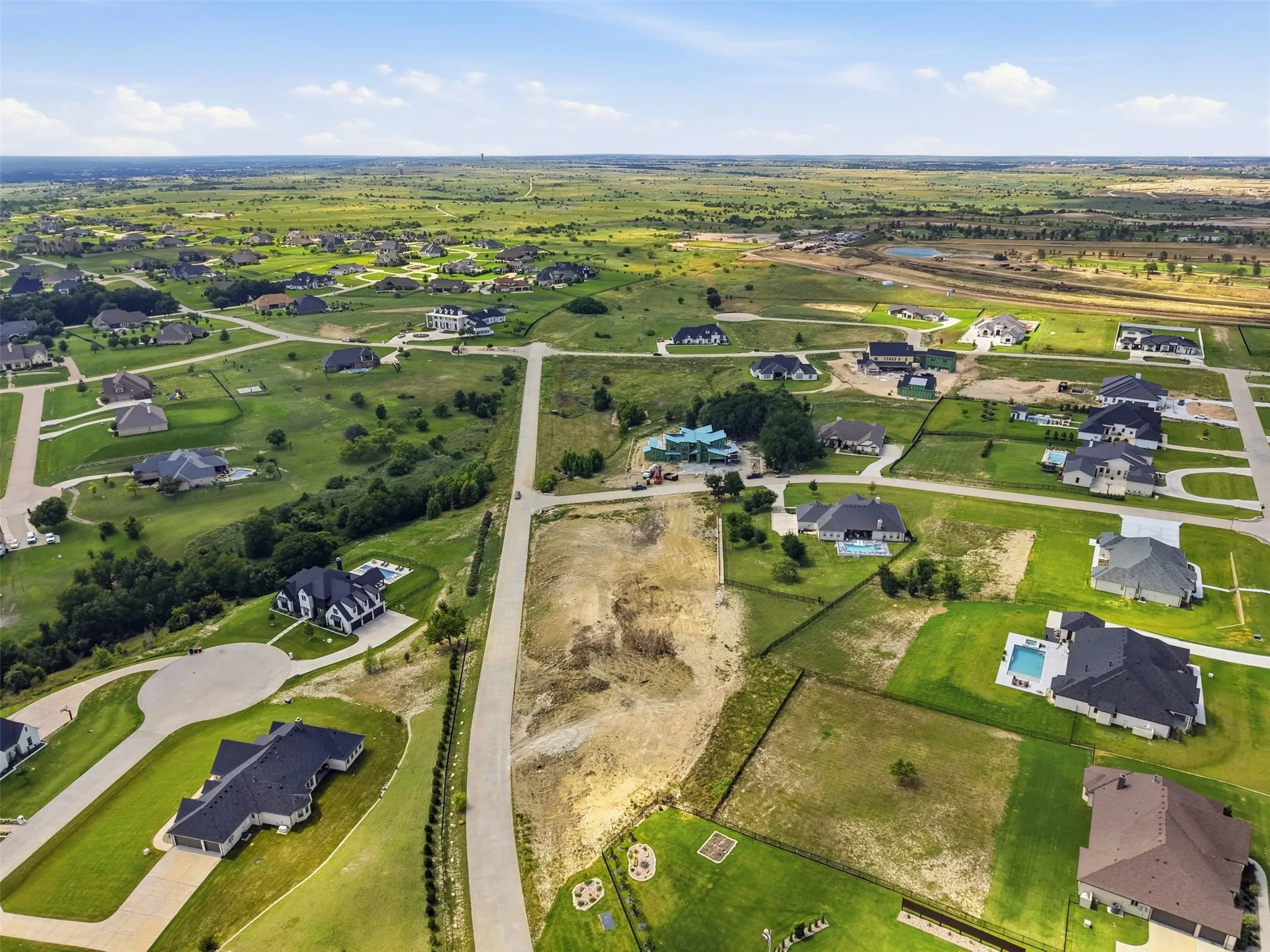 Expansive lot within a developed residential community, featuring paved roadways and surrounding properties with private swimming pools