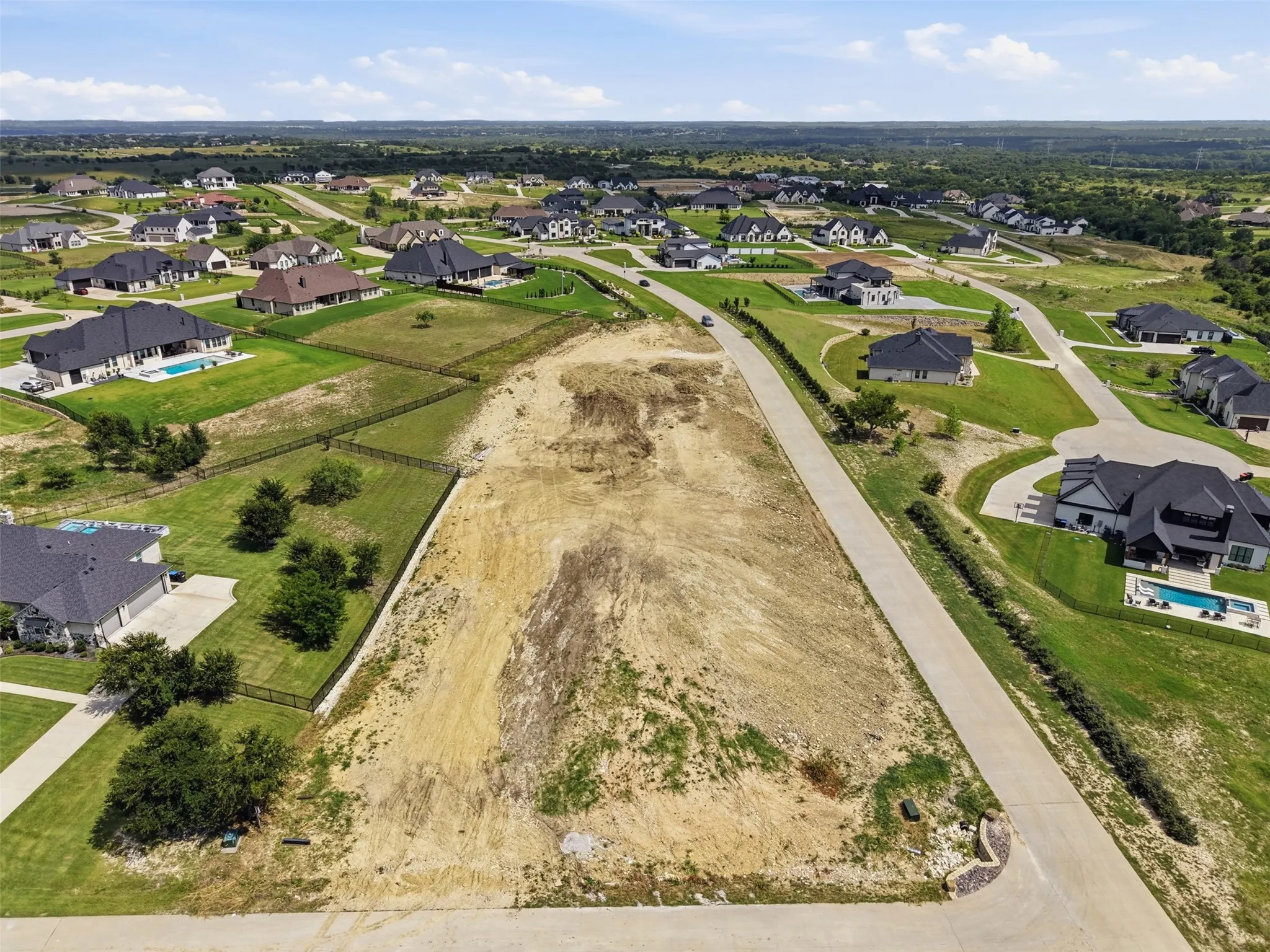 Expansive vacant lot with street frontage, surrounded by established residences, and featuring a partially cleared terrain