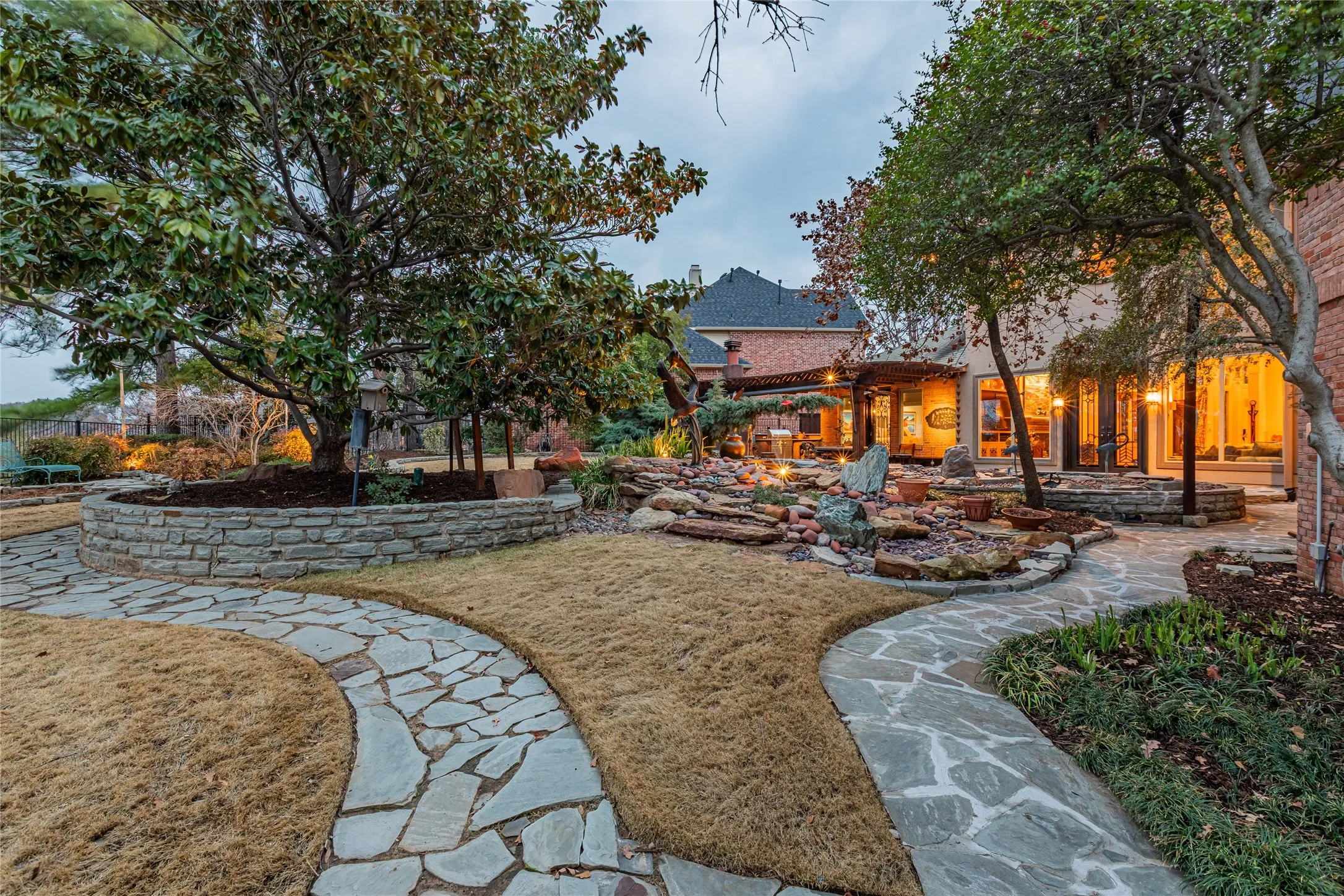 Extensive backyard featuring flagstone pathways, a stone-lined planter with mature trees, and a decorative rock garden