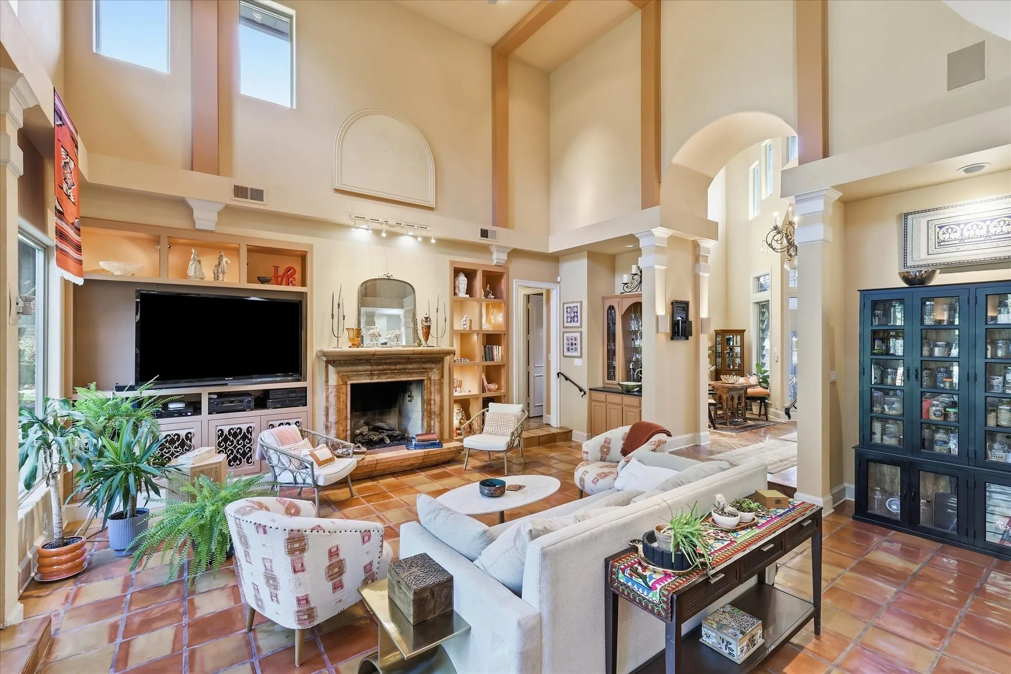 Living area featuring high ceilings, arched doorways, a stone fireplace, built-in cabinetry, and tile flooring