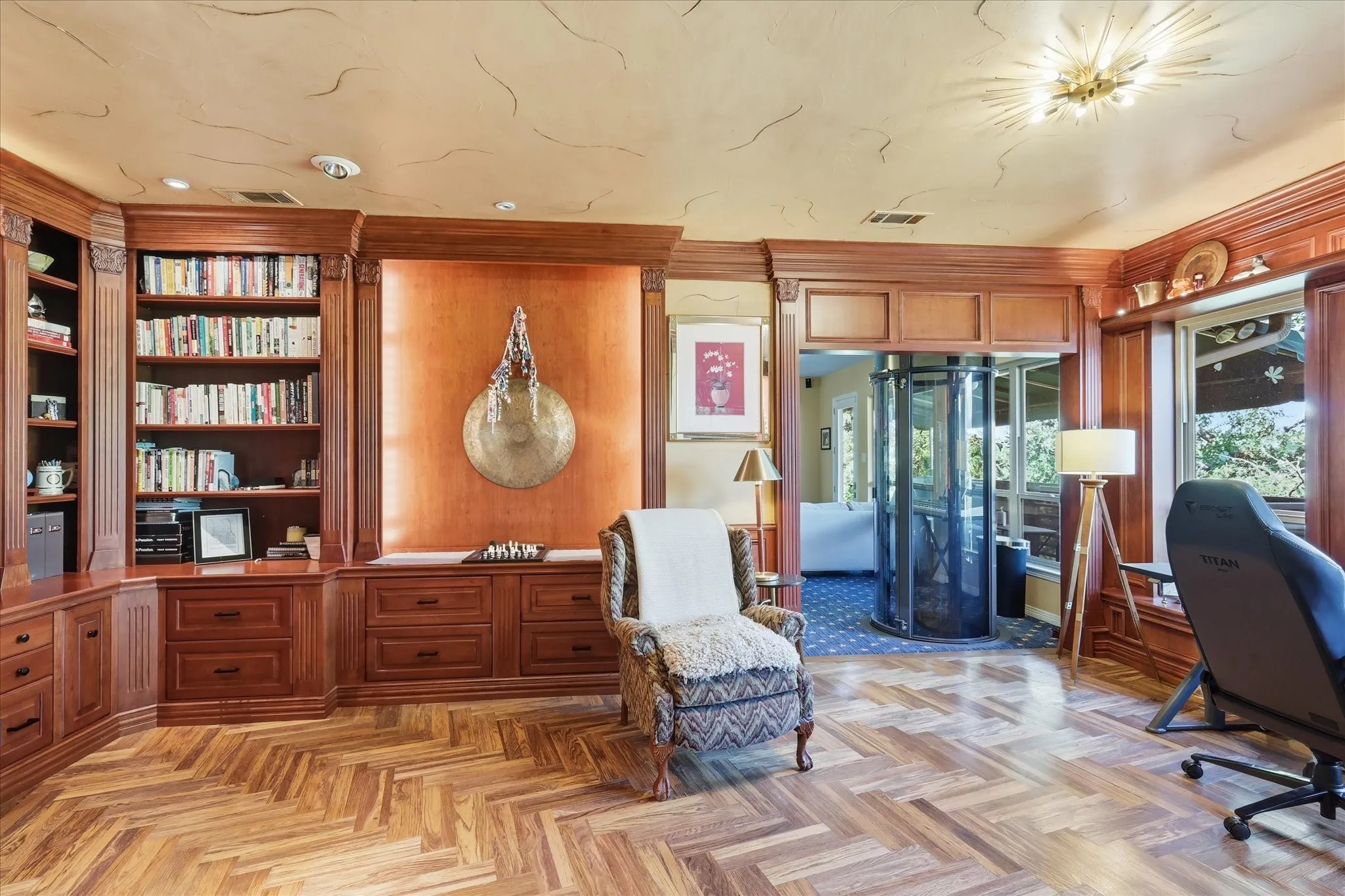Herringbone wood-finish flooring, extensive built-in custom cabinetry, built-in shelving, ornate crown molding, and an integrated cylindrical elevator
