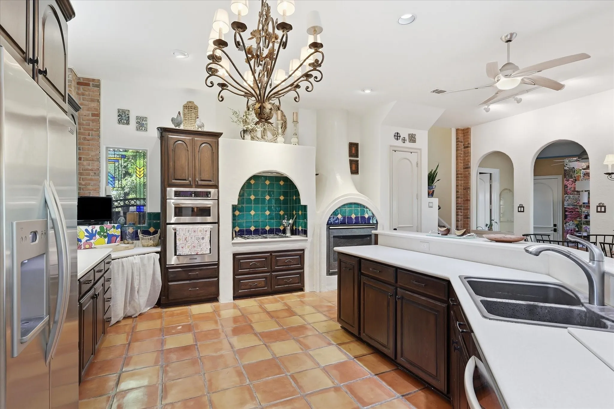 Kitchen featuring terracotta tile flooring, stainless steel appliances, dark wood cabinetry, a decorative tiled archway, and a ceiling fan