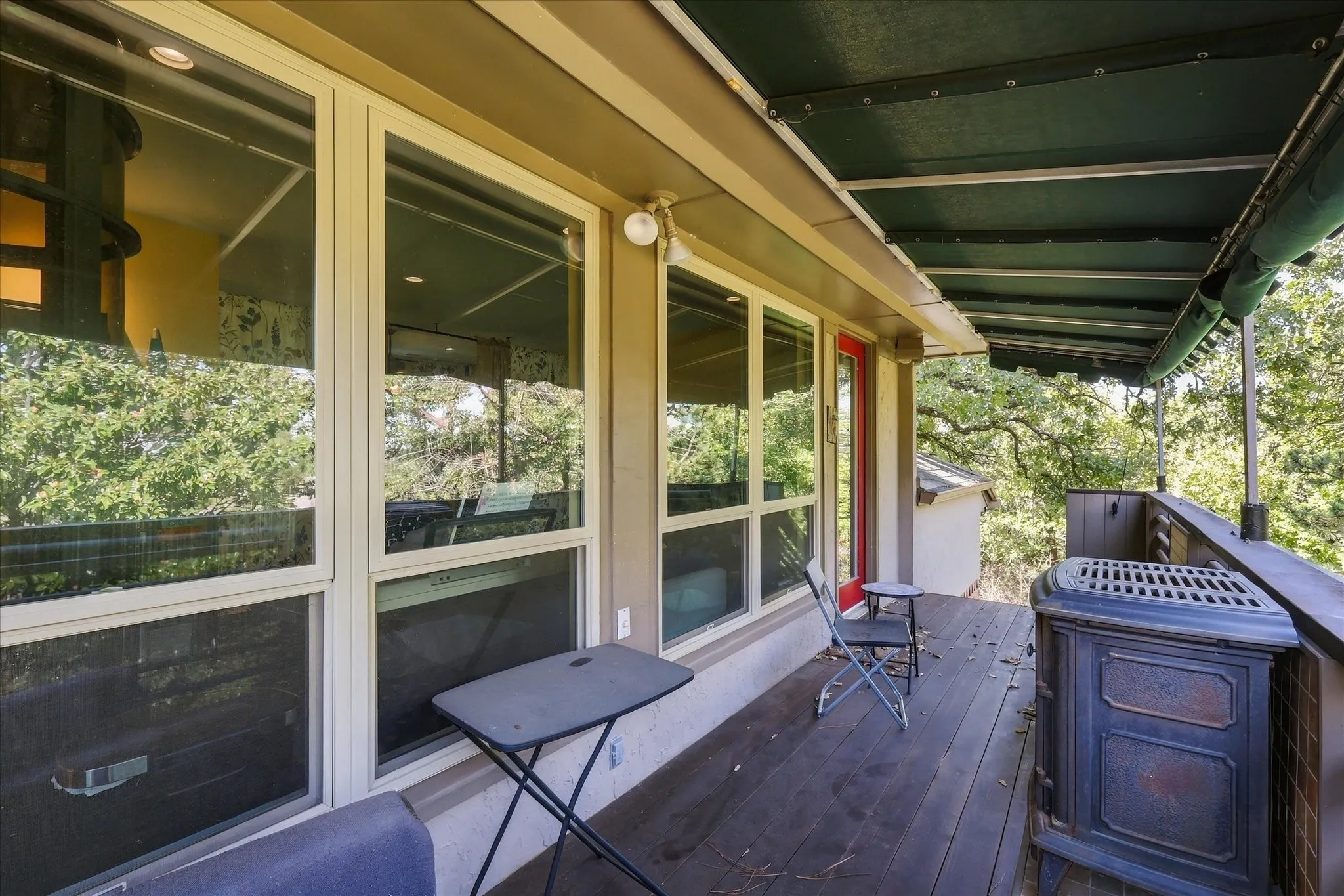 Expansive outdoor deck featuring wood-finish flooring, a fixed green awning, and large windows