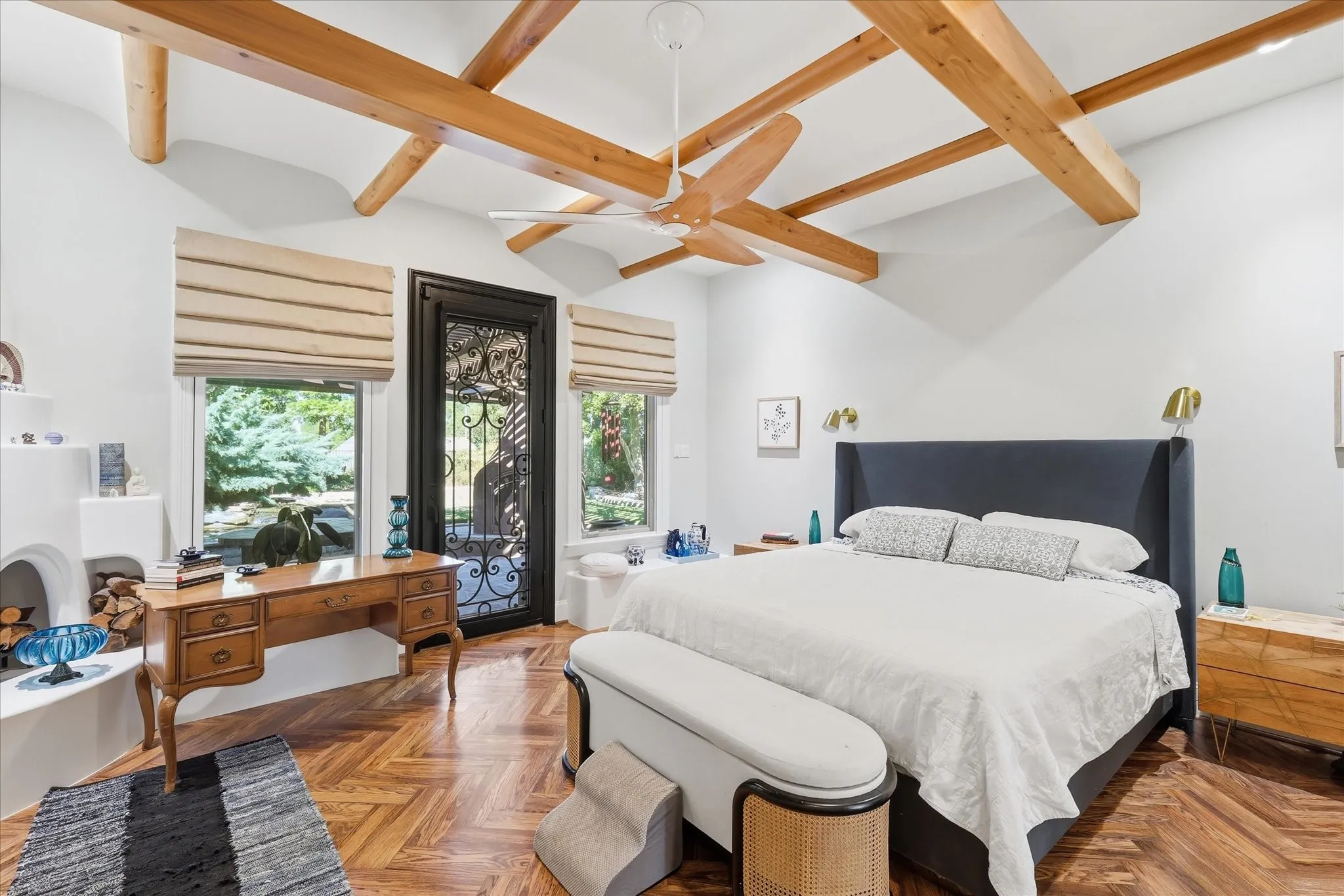 Vaulted ceiling with exposed wood beams, herringbone wood-finish flooring, a built-in kiva fireplace, and a decorative wrought iron door