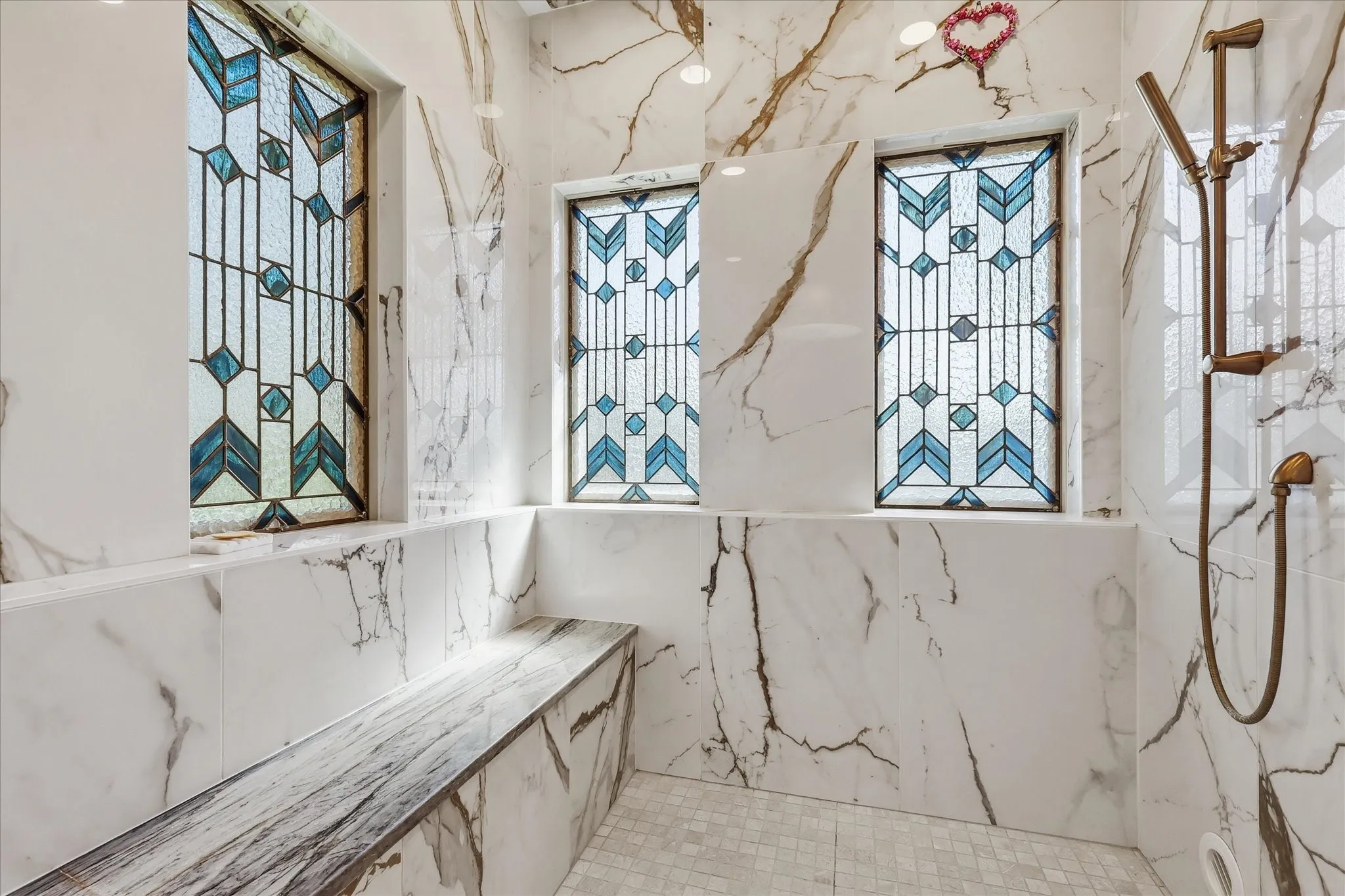 Walk-in shower with full-height marble-look tile, built-in bench, decorative stained-glass windows, and a bronze shower fixture