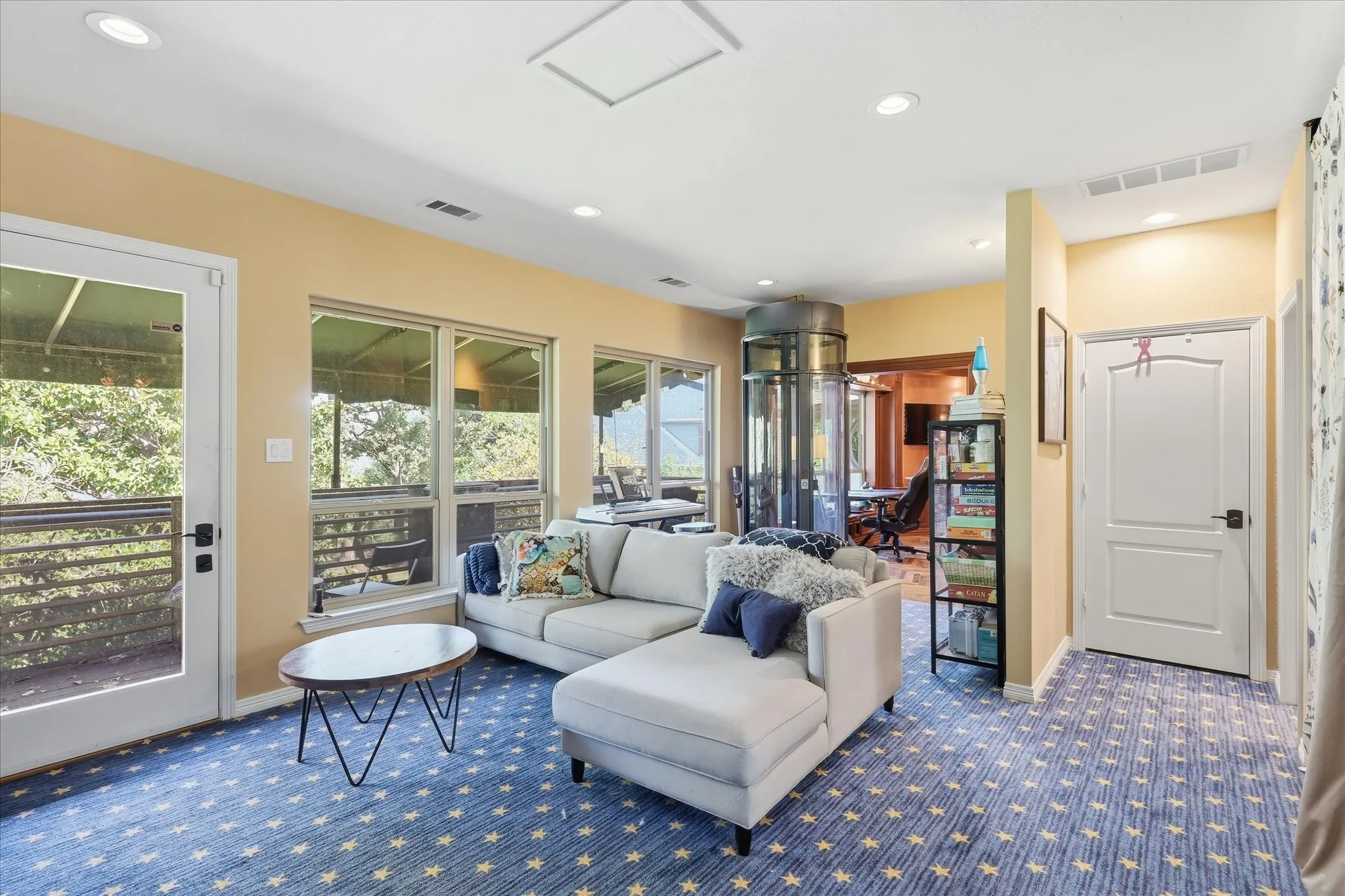 Spacious room featuring multiple windows, a glass-paneled door, recessed lighting, and a built-in circular elevator