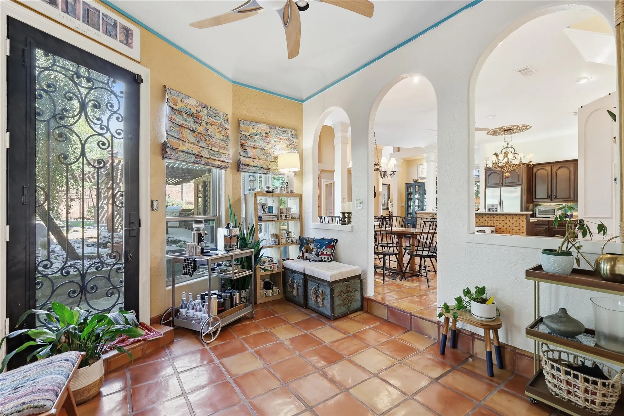 Terracotta tile flooring, decorative wrought iron door, arched doorways, ceiling fan, and cased openings