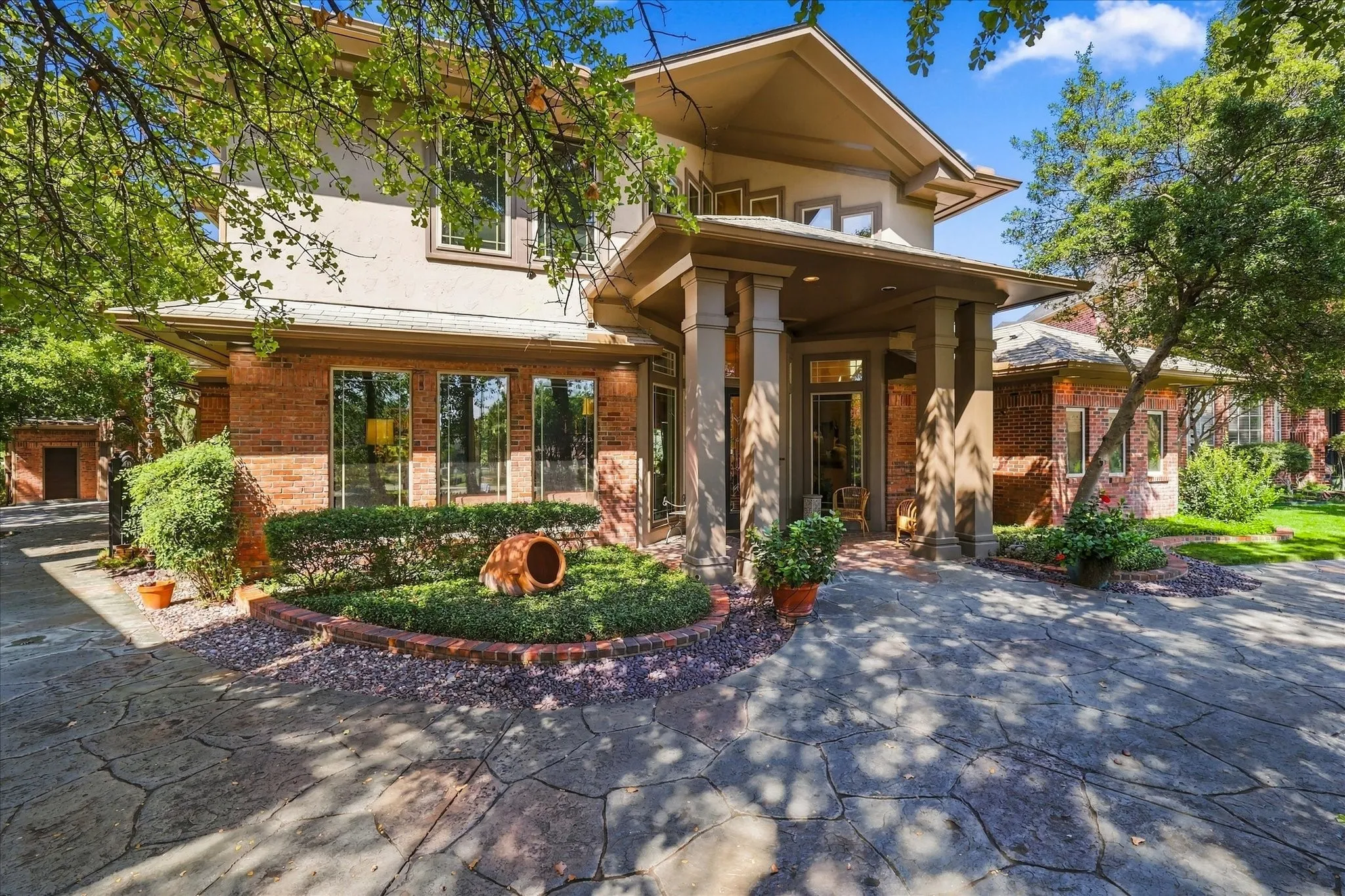 Stucco and brick exterior with multiple windows, a covered entry with columns, and a stamped concrete driveway