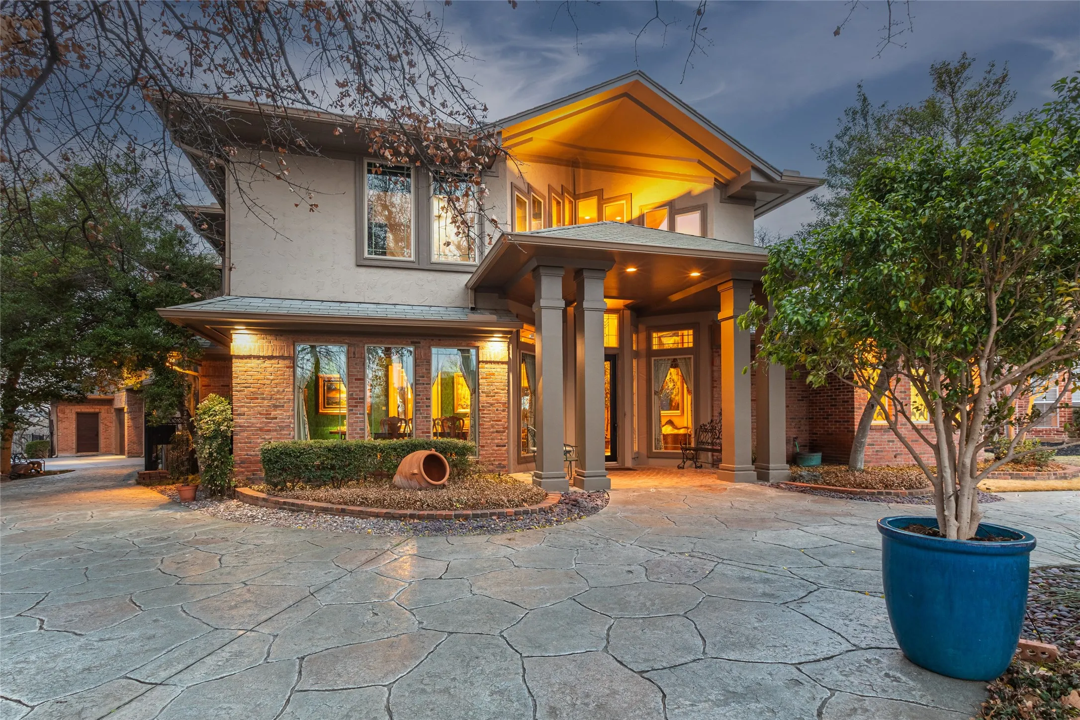 Stucco and brick exterior with multiple window styles, covered entryway, prominent columns, and a stamped concrete driveway