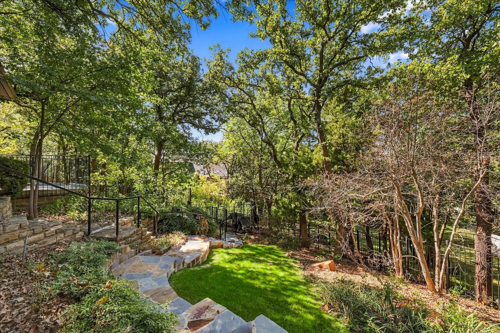 Stone steps with flagstone path, wrought iron railings, manicured lawn, and mature trees