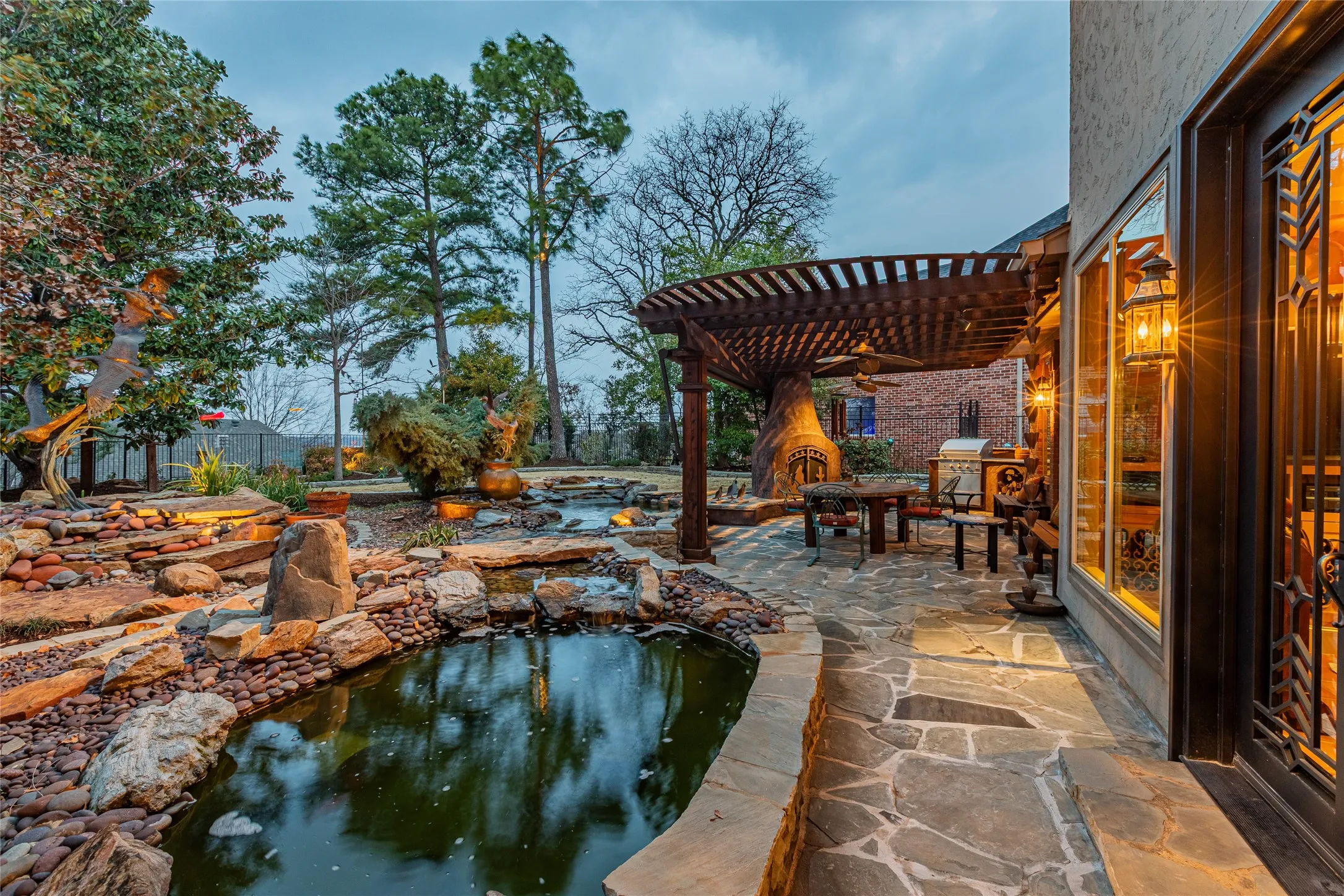 Stone patio with a wood pergola, built-in outdoor fireplace, and a water feature with rock landscaping