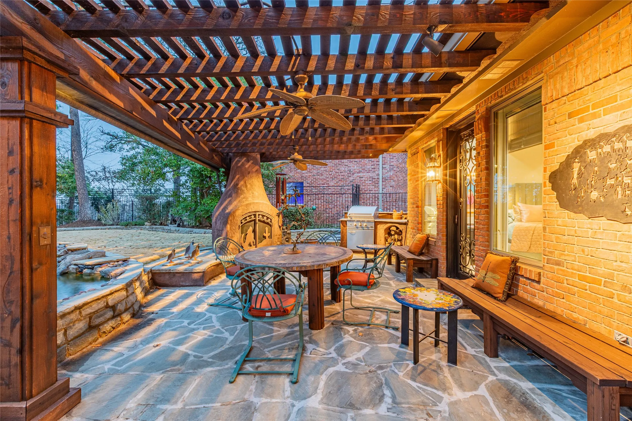 Expansive stone patio with a wood pergola, built-in outdoor kitchen, stone fireplace, and a water feature