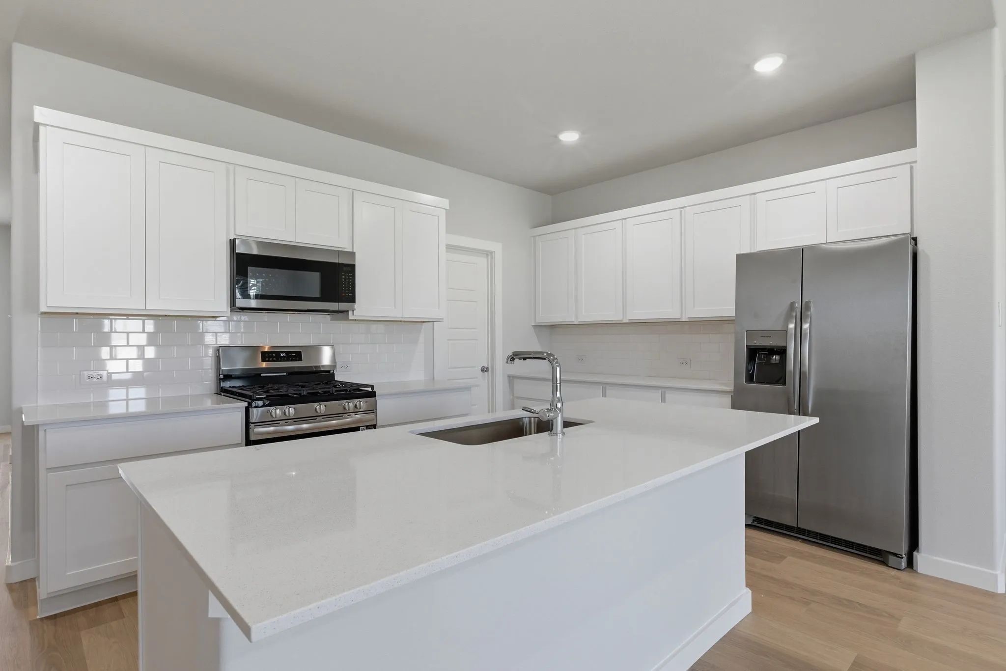 Kitchen featuring white shaker cabinetry, white subway tile backsplash, stainless steel appliances, and a central island with a sink and a gooseneck faucet