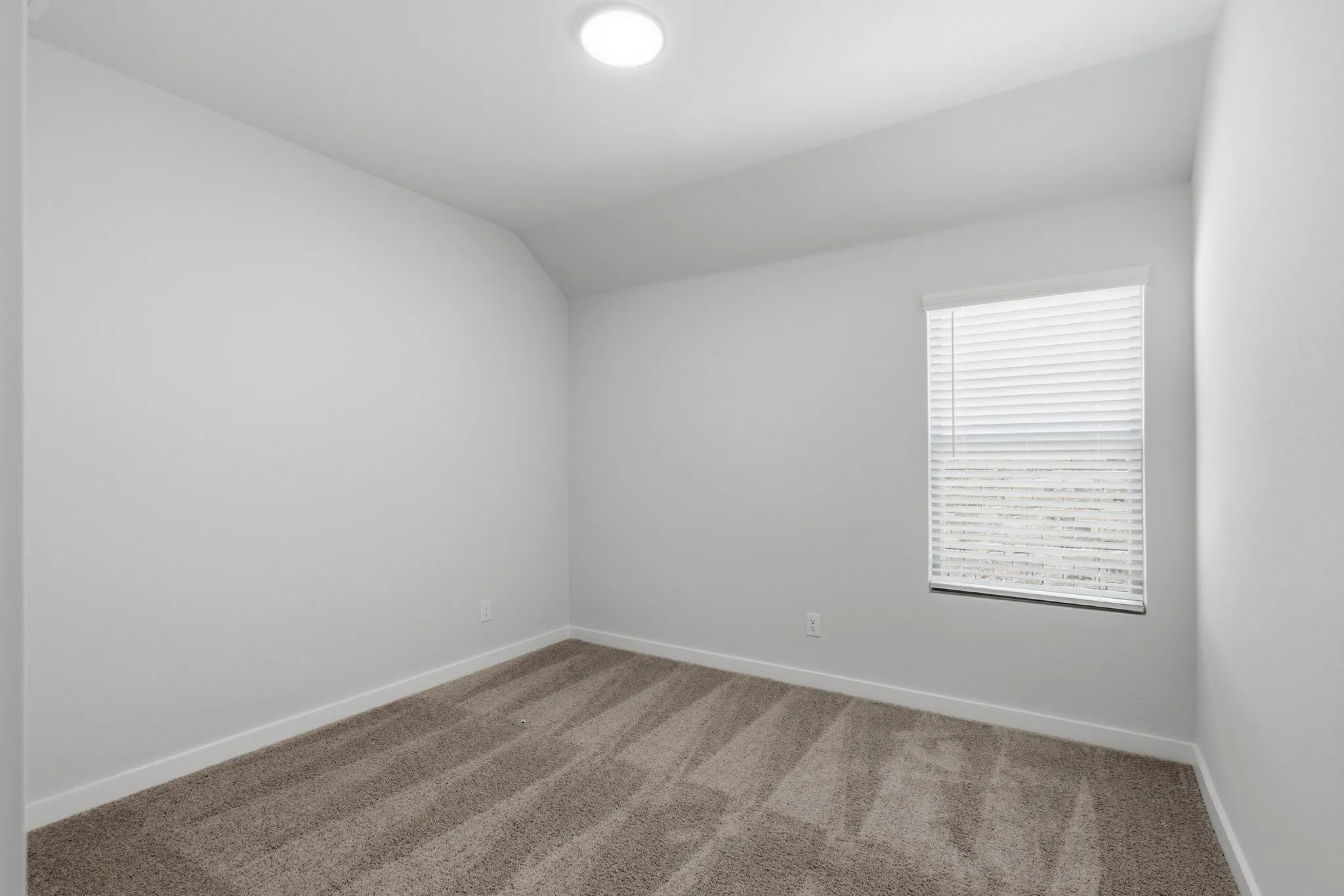 Recessed ceiling lighting, white walls, carpeted flooring, and a single window with blinds