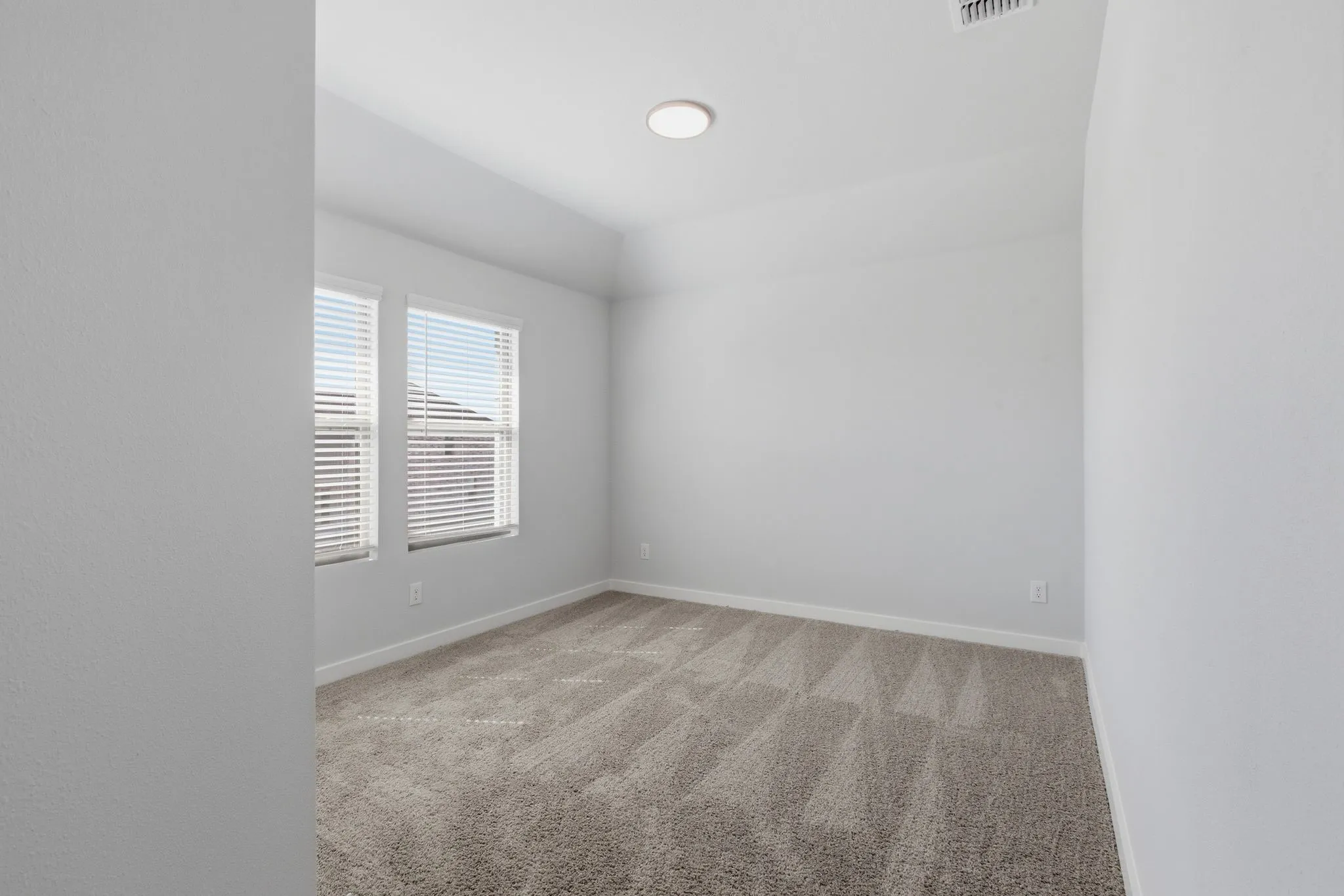 Recessed ceiling light, neutral tone walls, carpeted flooring, two windows with blinds