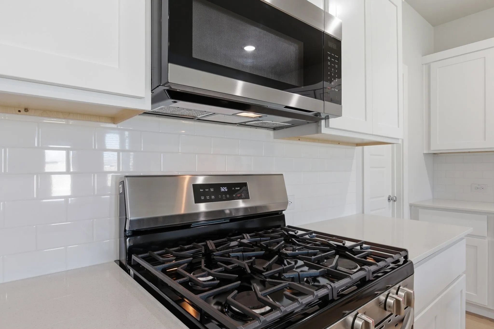 Stainless steel gas range with a matching microwave, white subway tile backsplash, white shaker-style cabinetry, and light-toned countertops