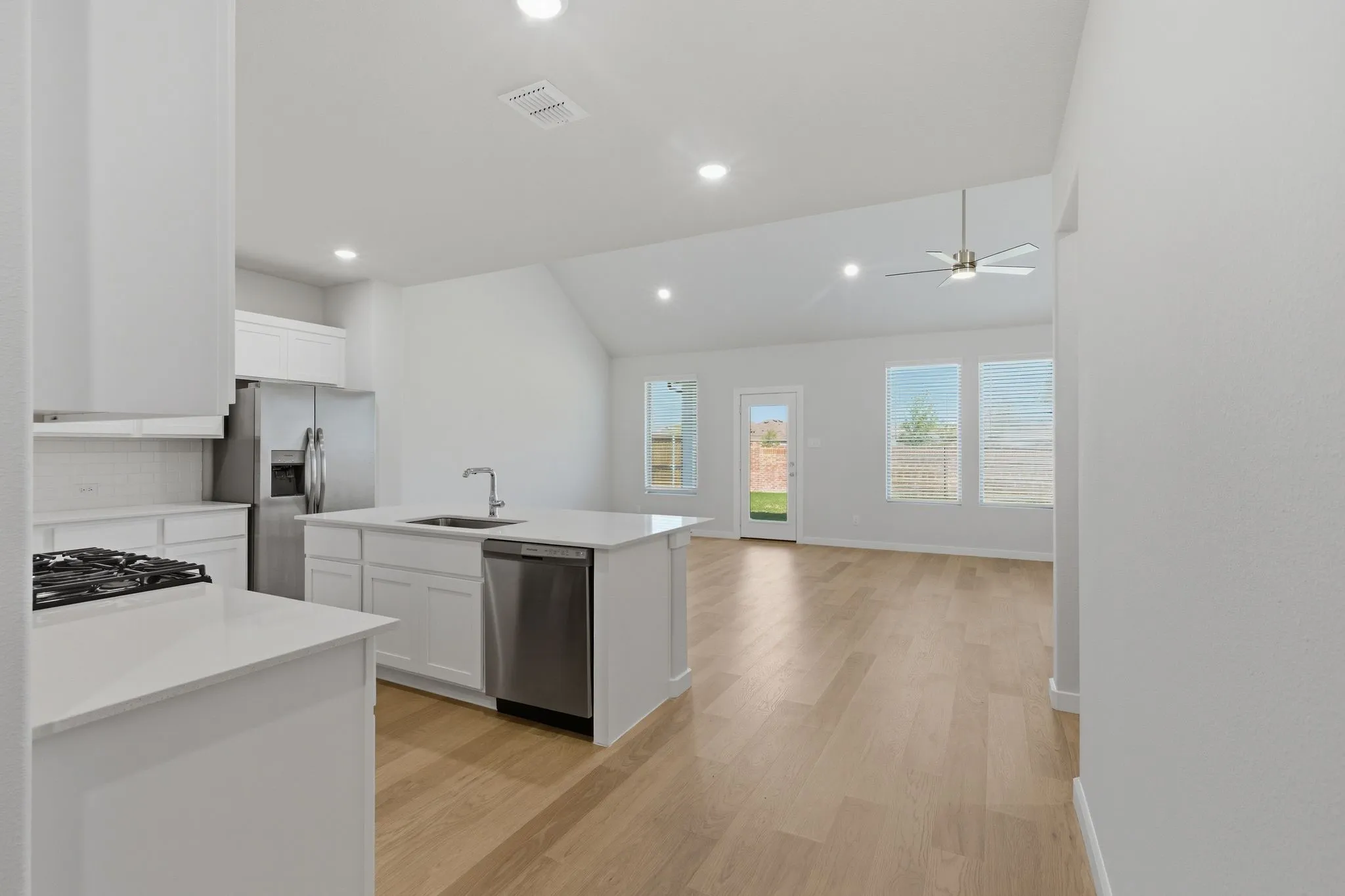 Modern kitchen featuring white cabinetry, stainless steel appliances, an island with an integrated sink, and light wood-finish flooring
