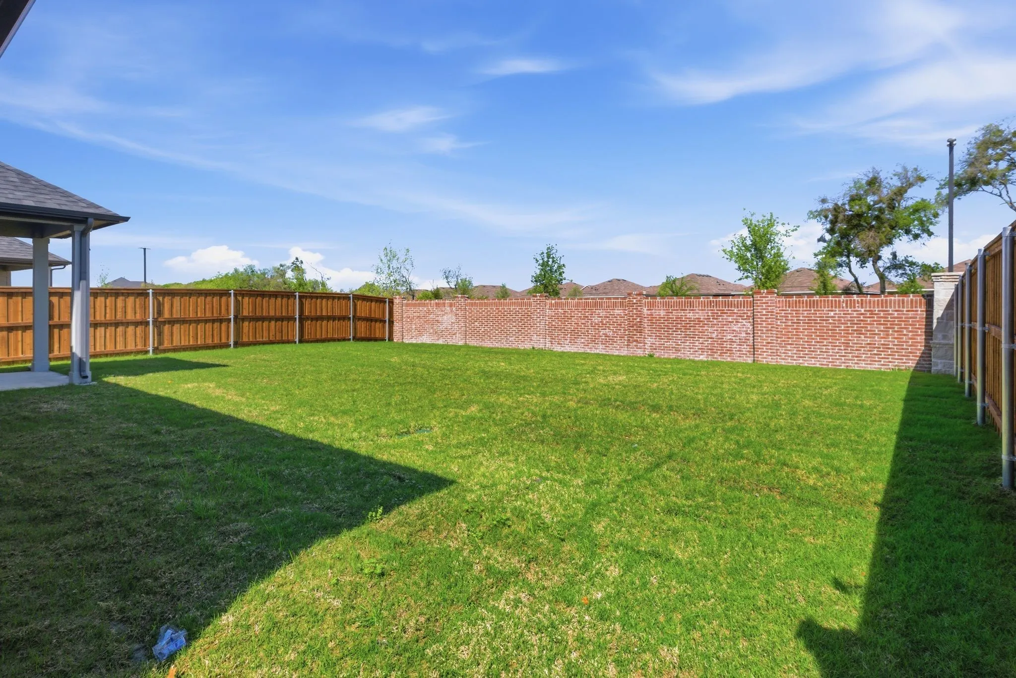 Expansive lawn with wood privacy fencing and a brick perimeter wall, featuring a covered patio