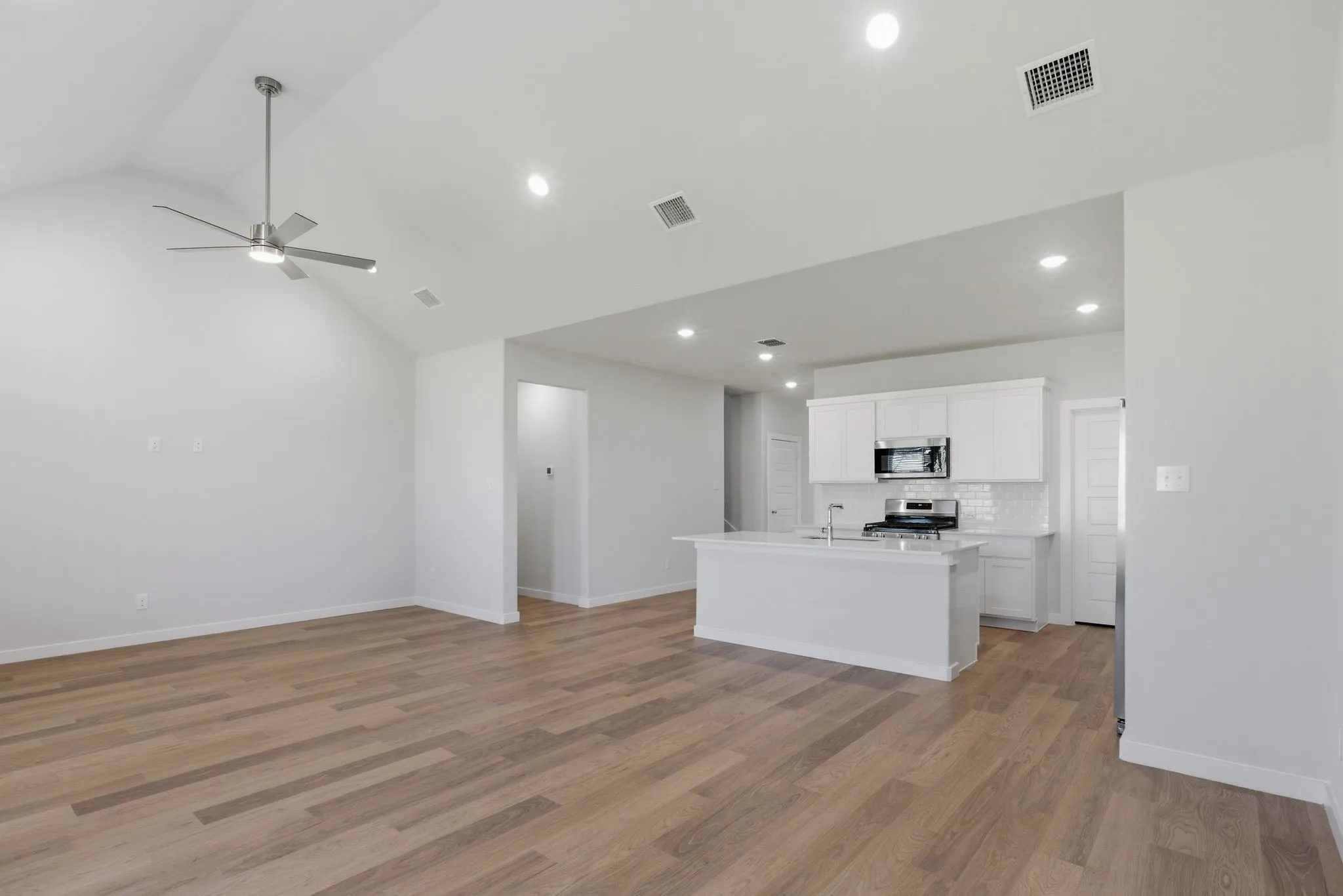 Vaulted ceiling with a ceiling fan, recessed lighting, wood-finish flooring, white kitchen cabinetry, and stainless steel appliances