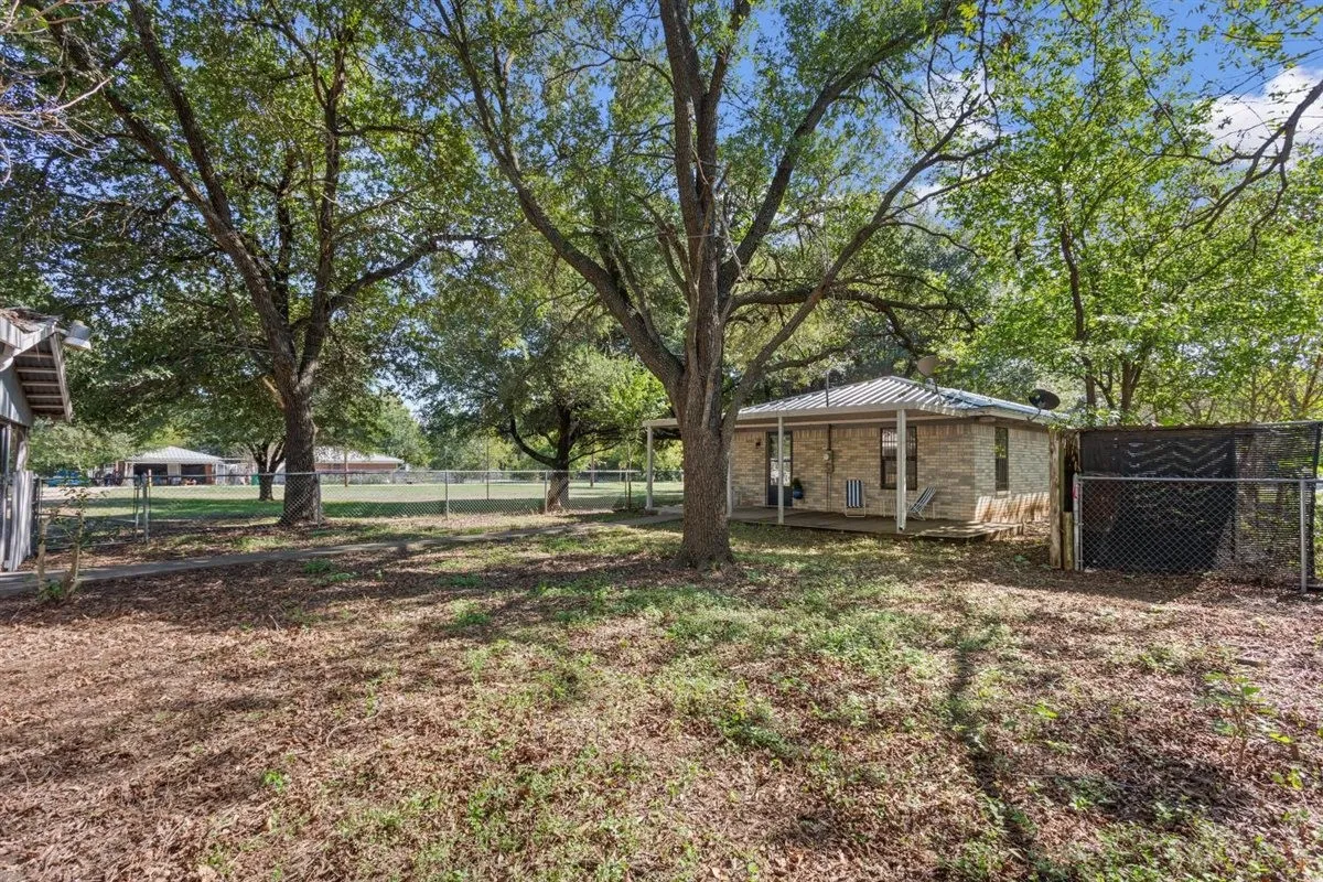 Expansive outdoor space featuring mature trees, a chain-link fence, and a brick-sided structure with a covered porch