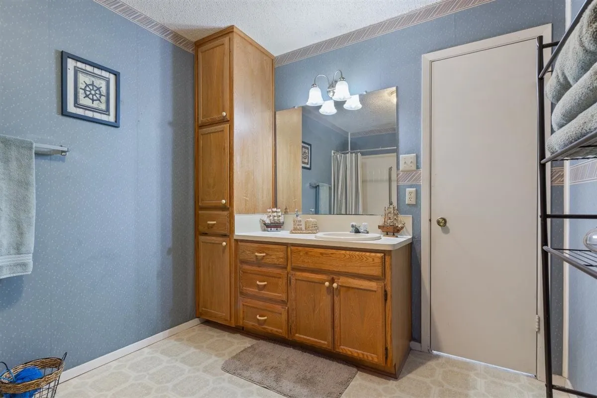 Extended height wood-finish cabinetry, wood-finish vanity with drawer and cabinet storage, single basin sink, wall-mounted vanity mirror, and overhead sconce lighting