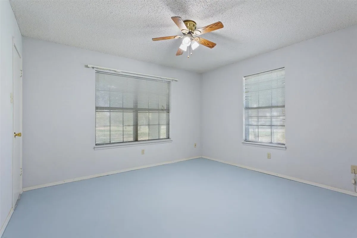 Wood-blade ceiling fan with integrated lighting, two windows with blinds, and light blue flooring