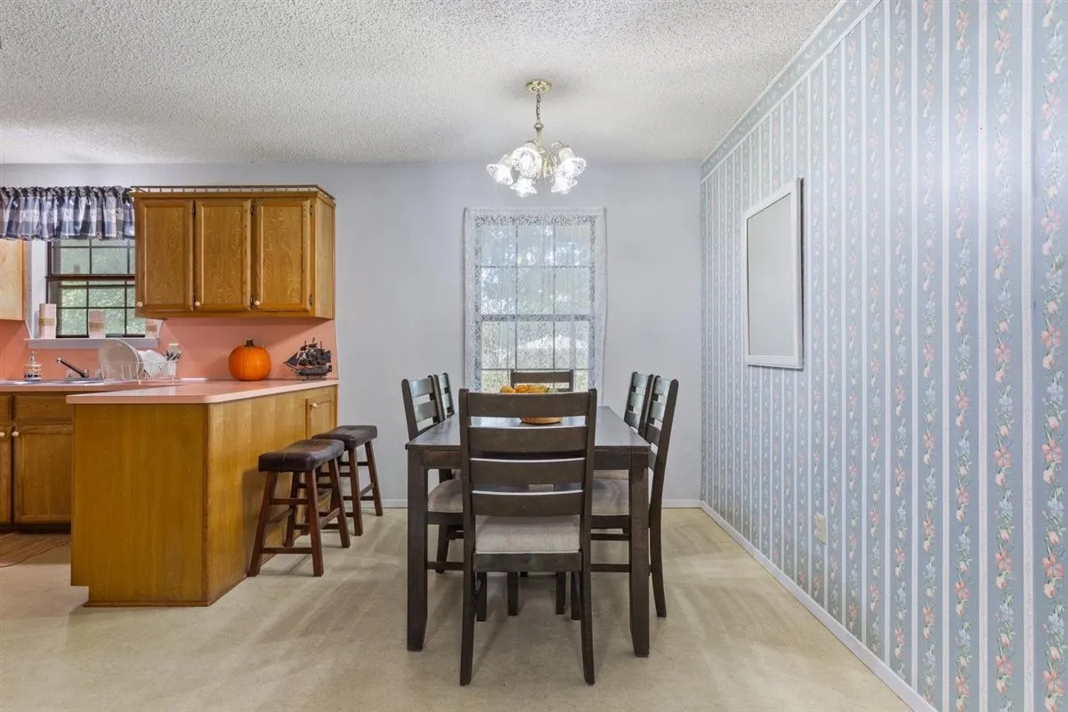 Kitchen cabinetry with a breakfast bar, patterned wallpaper accent wall, and a dining area with overhead lighting