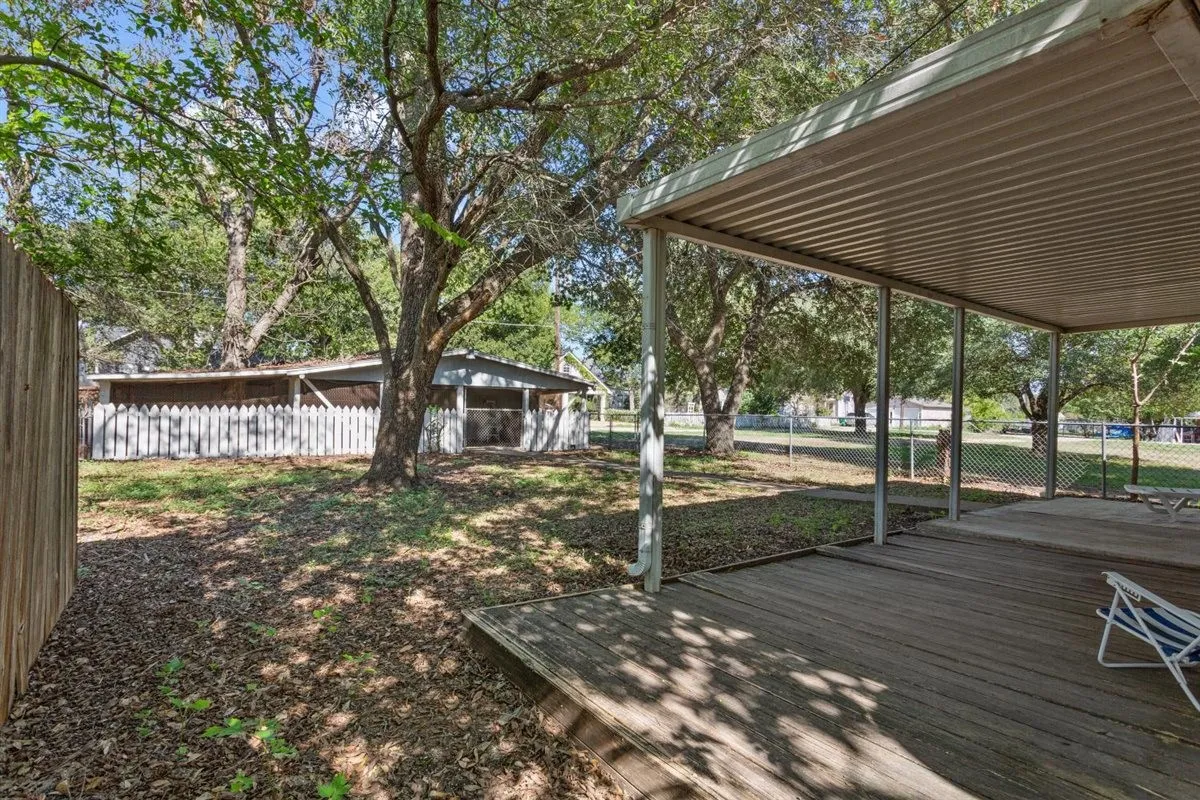 Expansive backyard featuring a covered wood-deck patio, mature trees, a wooden privacy fence, and a white picket fence