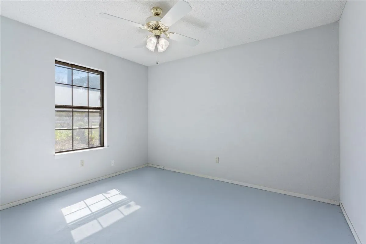 Smooth wall finishes, grid-pattern window, ceiling fan with integrated lighting, and light-toned flooring