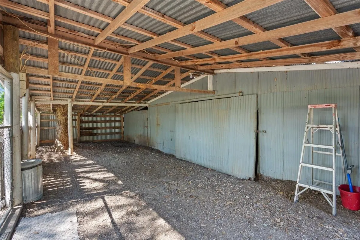 Open-air structure with exposed wood beam ceiling, corrugated metal roofing, and gravel flooring