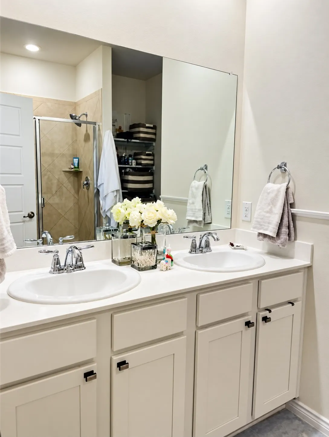 Dual undermount sinks with chrome fixtures, white countertops, and white cabinetry