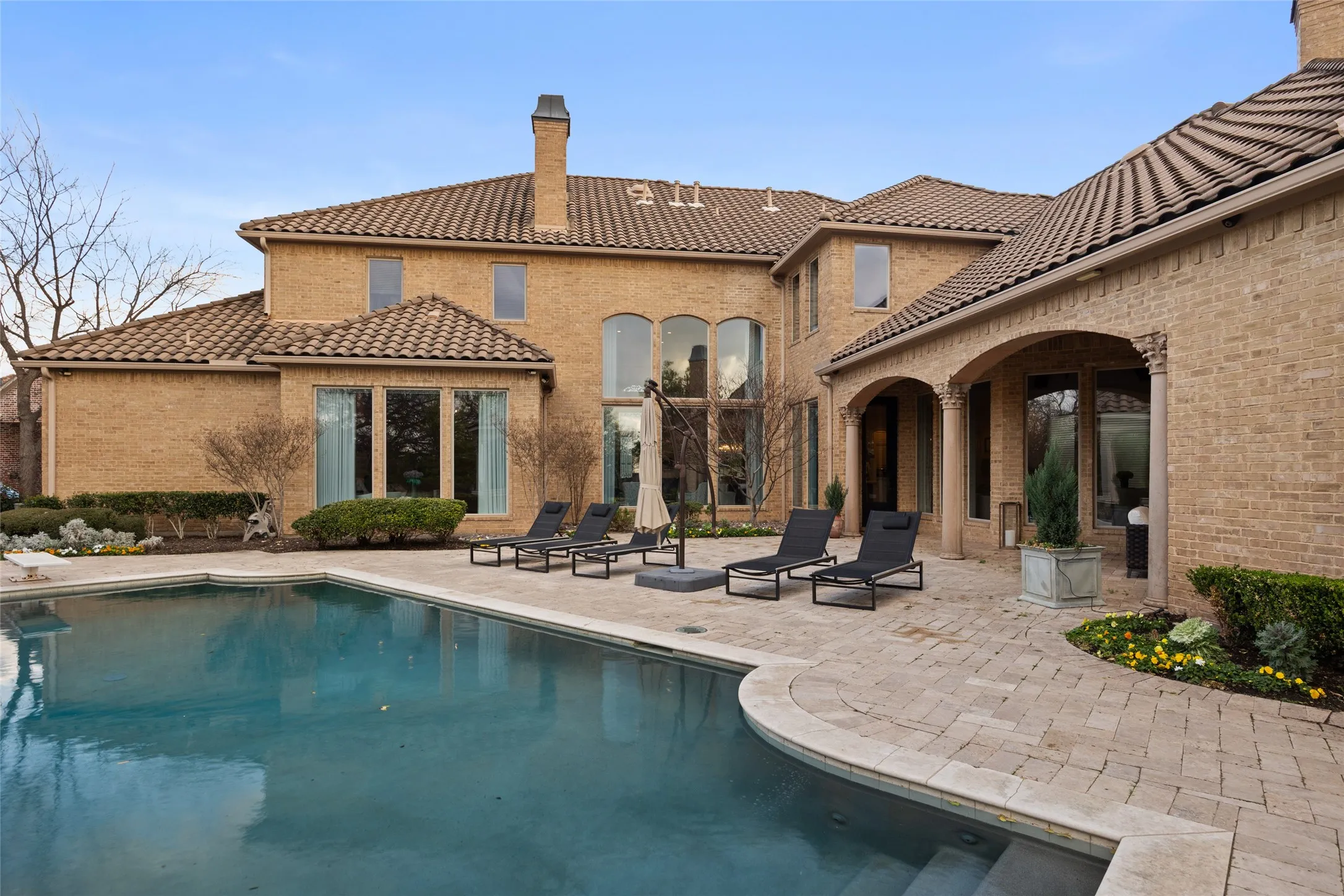 Exterior featuring a swimming pool, spacious patio, brick facade, arched entryways, and multiple windows