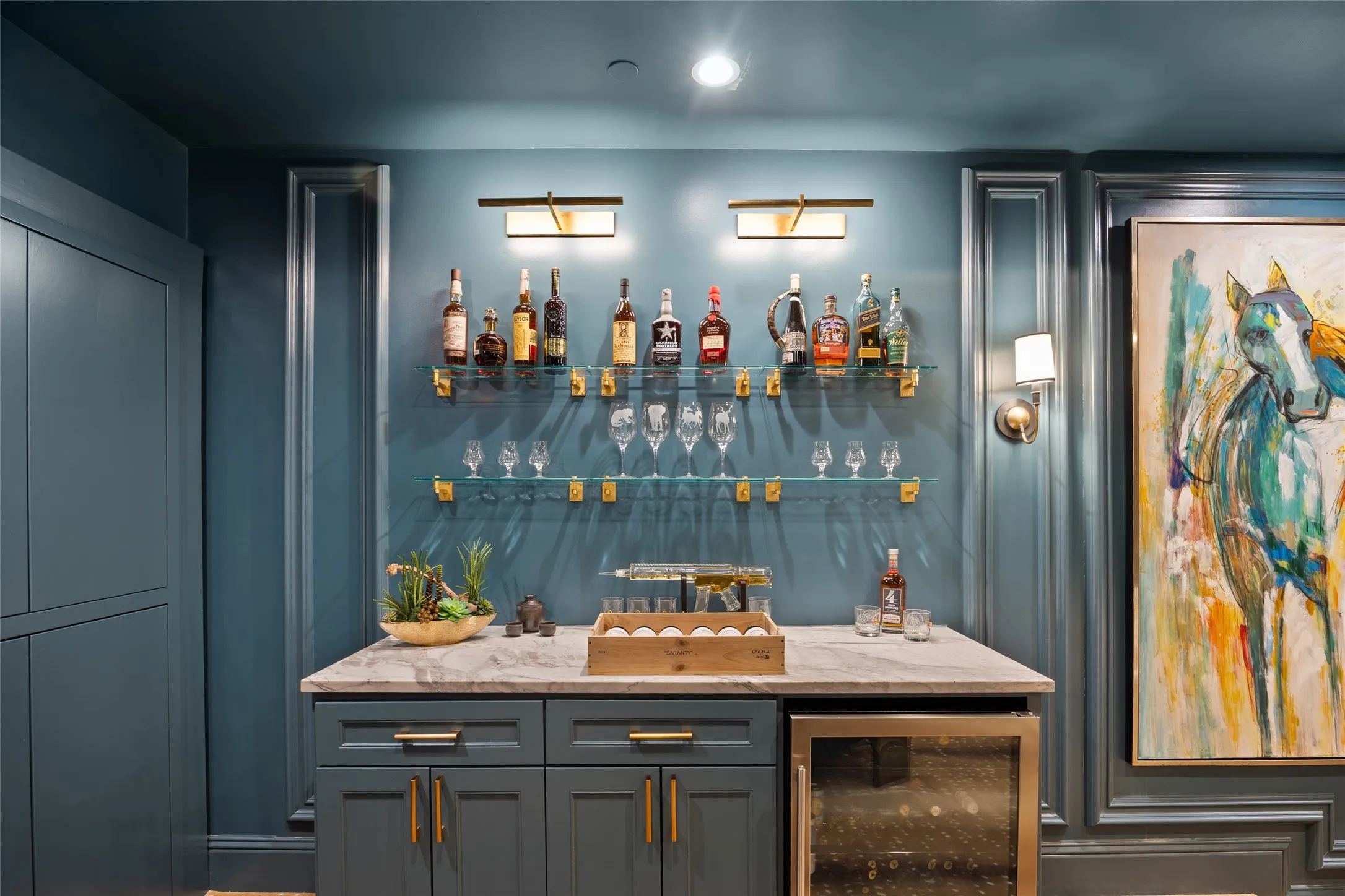 Built-in wet bar featuring a stone countertop, under-counter beverage refrigerator, custom cabinetry with brass hardware, and glass shelving