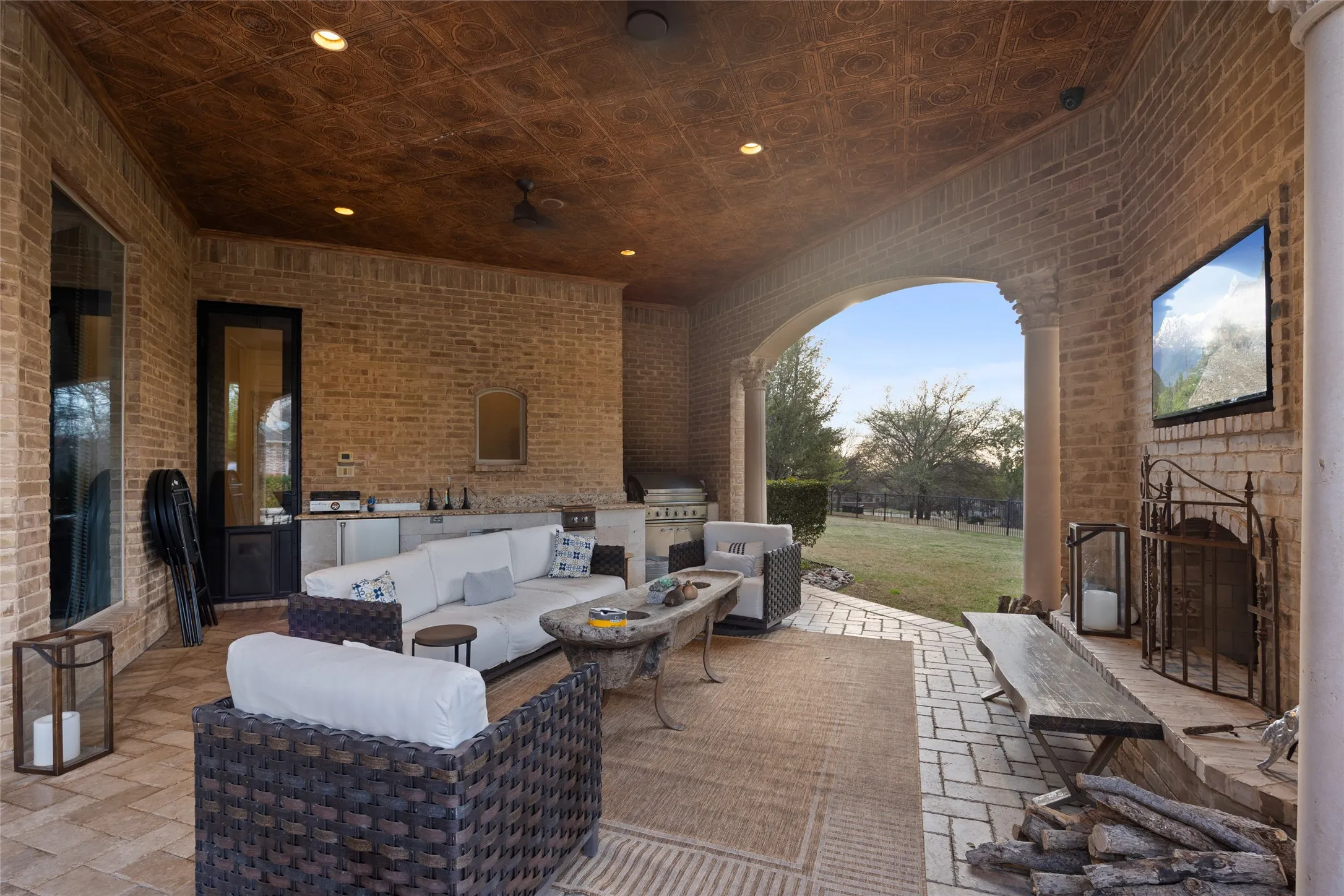 Expansive covered patio featuring a brick exterior, recessed lighting, and a built-in outdoor kitchen with stainless steel appliances