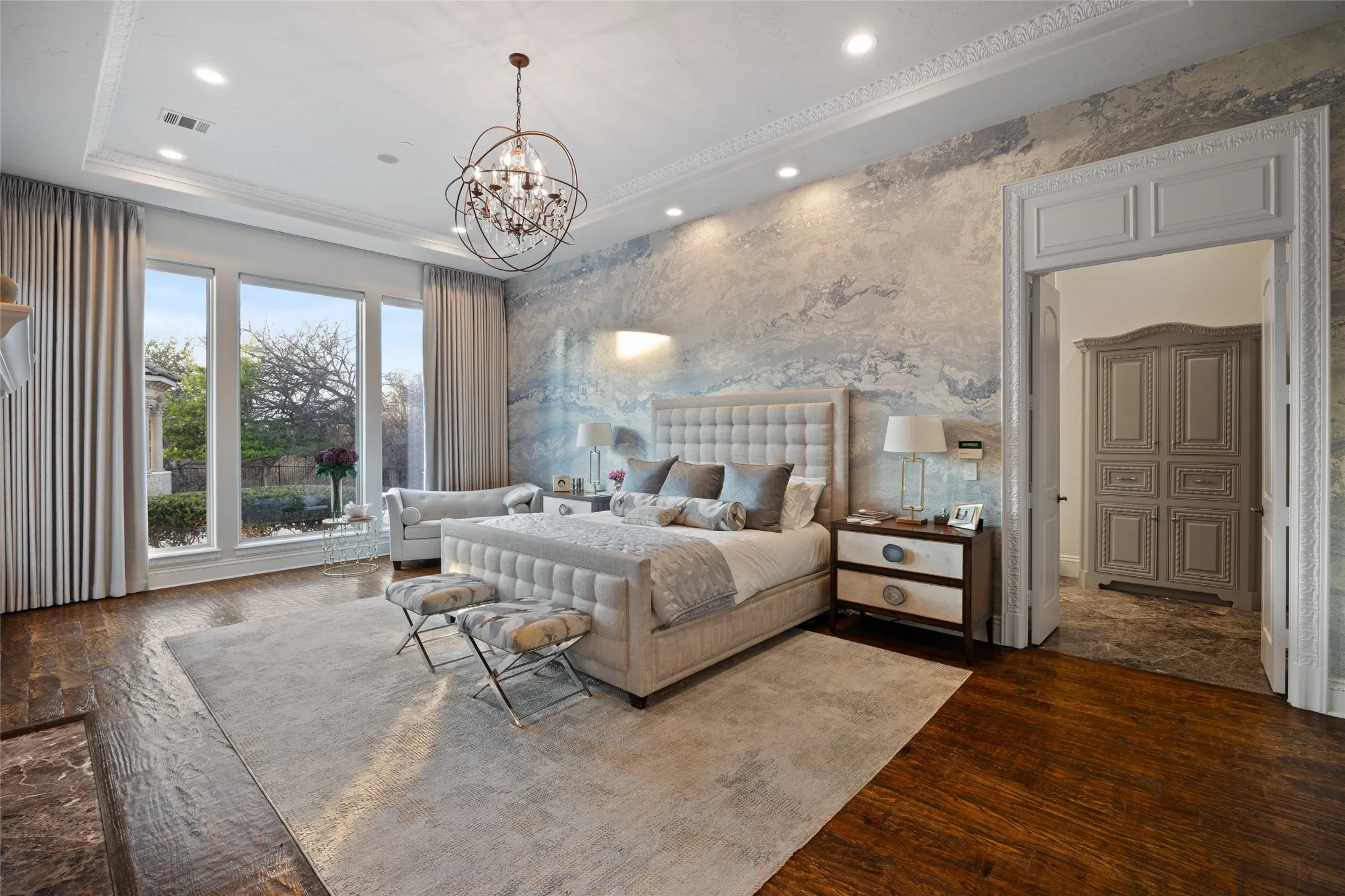 Hardwood flooring, tray ceiling with recessed lighting, detailed crown molding, custom wall treatment, and an ornate chandelier