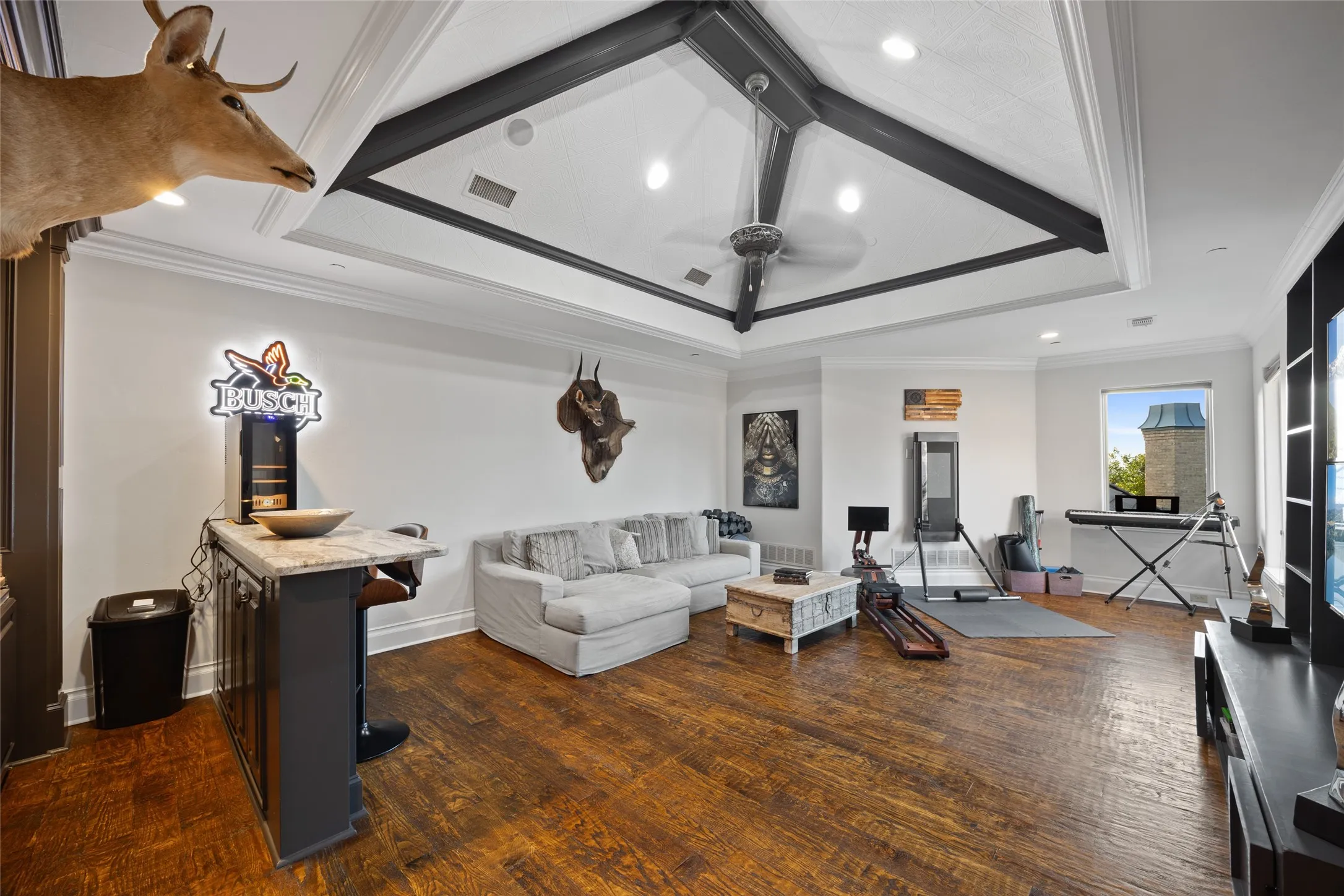 Spacious room featuring wood-finish flooring, a built-in wet bar with a stone countertop, a tray ceiling with exposed beams, and a ceiling fan