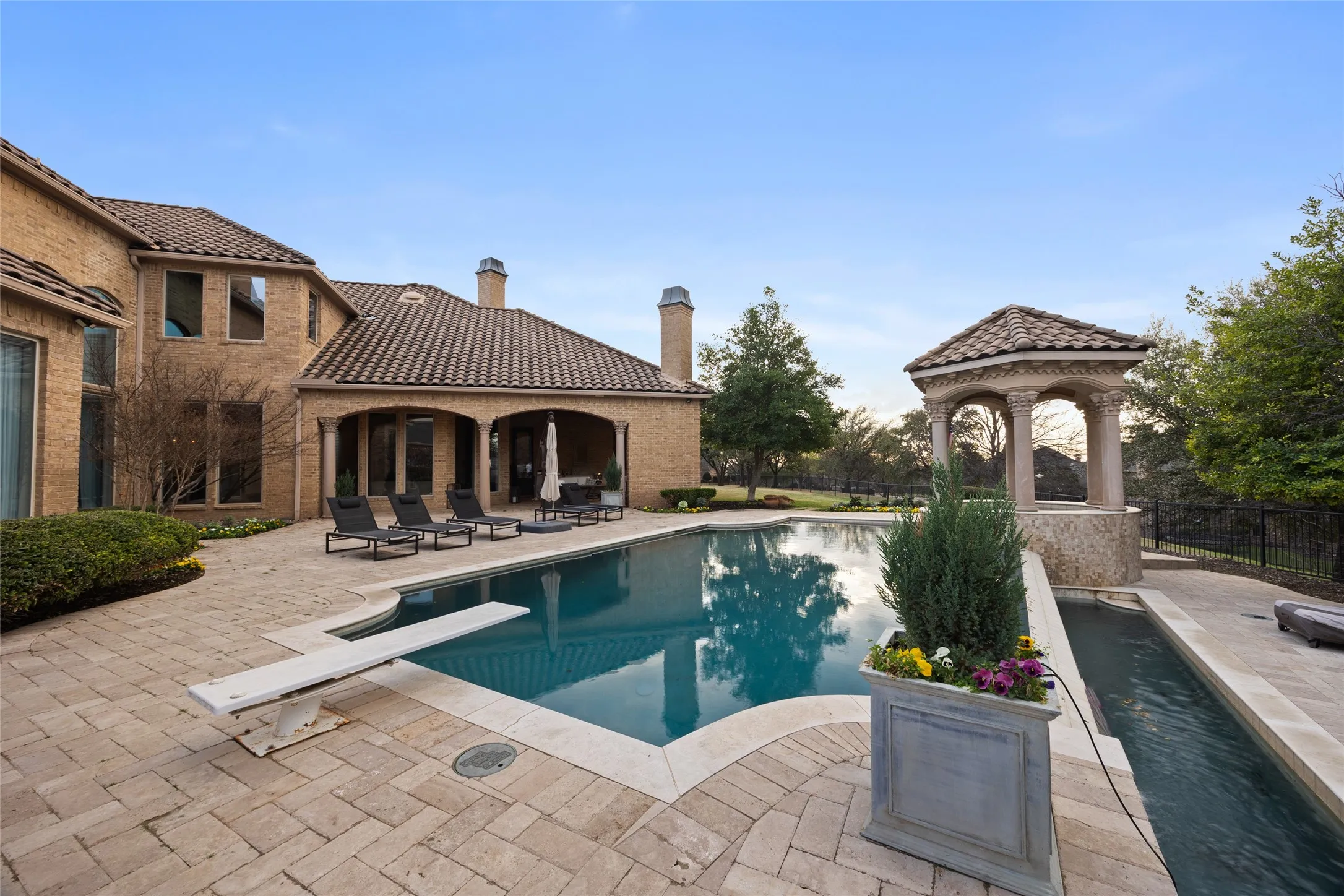 Expansive outdoor living area featuring a swimming pool with a diving board, surrounding paver patio, covered porch, and a stone gazebo