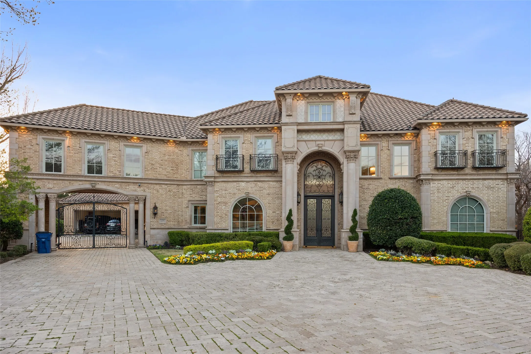 Mediterranean-style exterior featuring a tile roof, brick facade, arched entry, decorative iron double doors, and a paver driveway